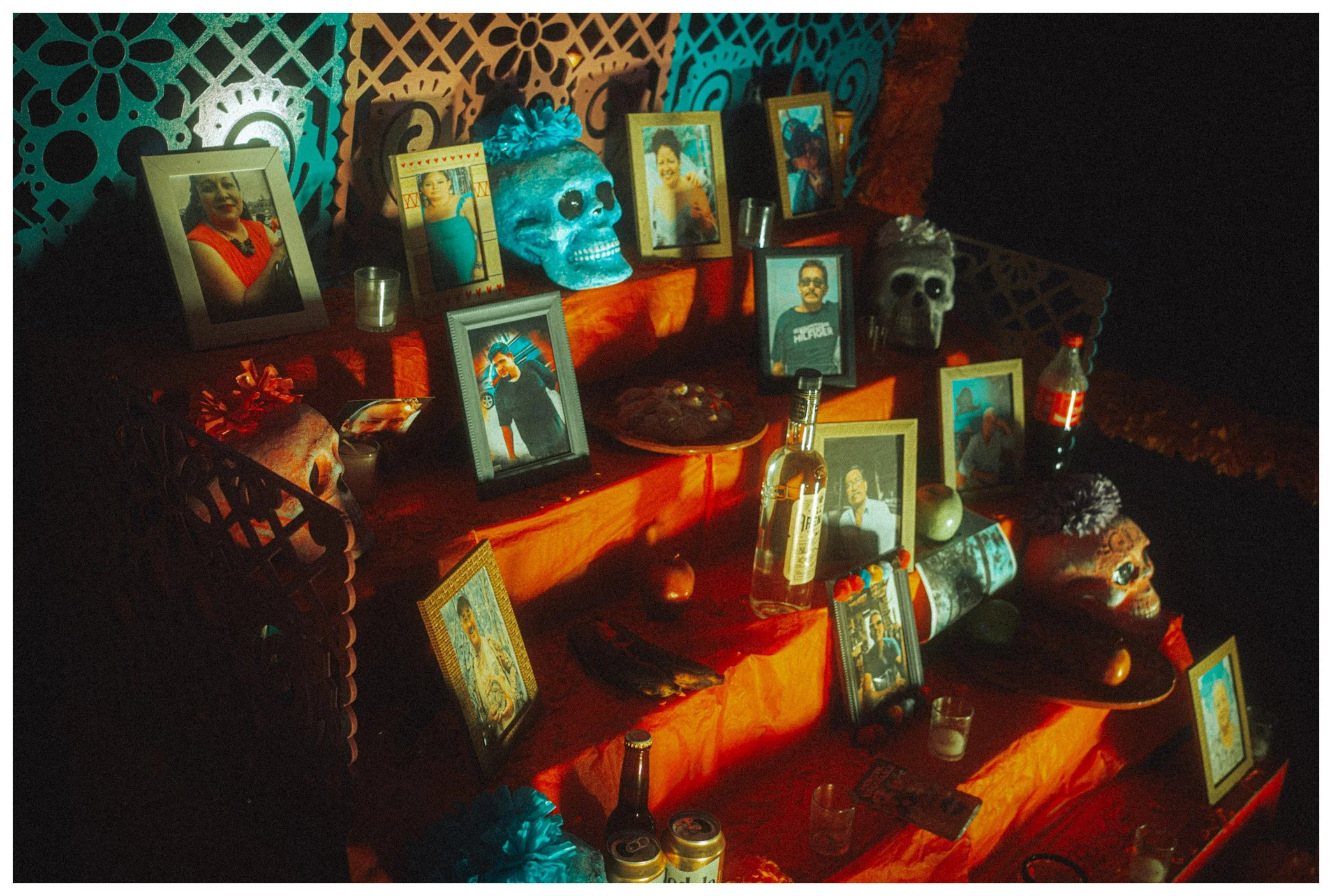 This image depicts a traditional Mexican Day of the Dead altar with framed photographs of loved ones, skull decorations, candles, and marigolds, illuminated with warm lighting.