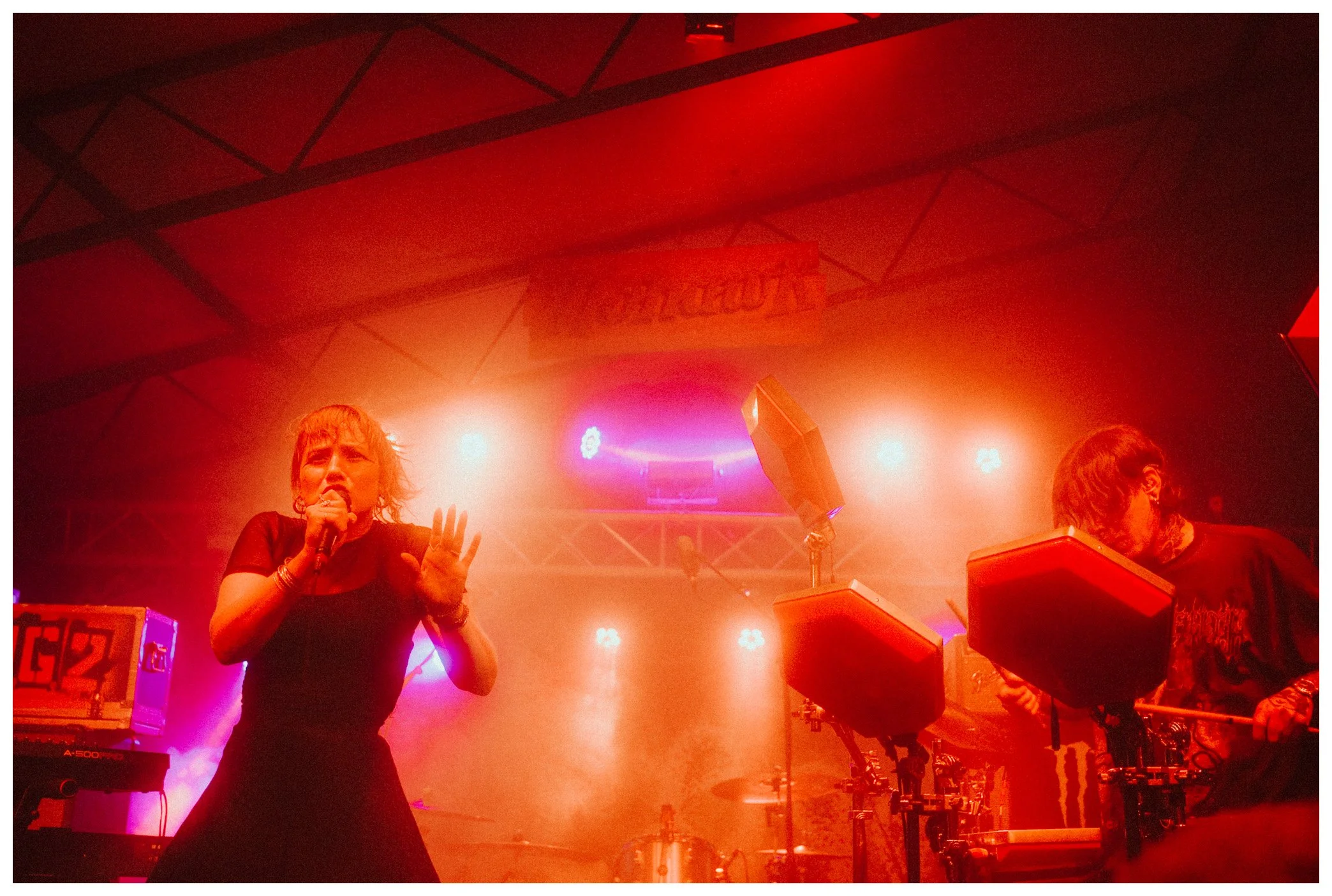 A woman singing into a microphone on stage with colorful stage lights and a neon sign in the background.