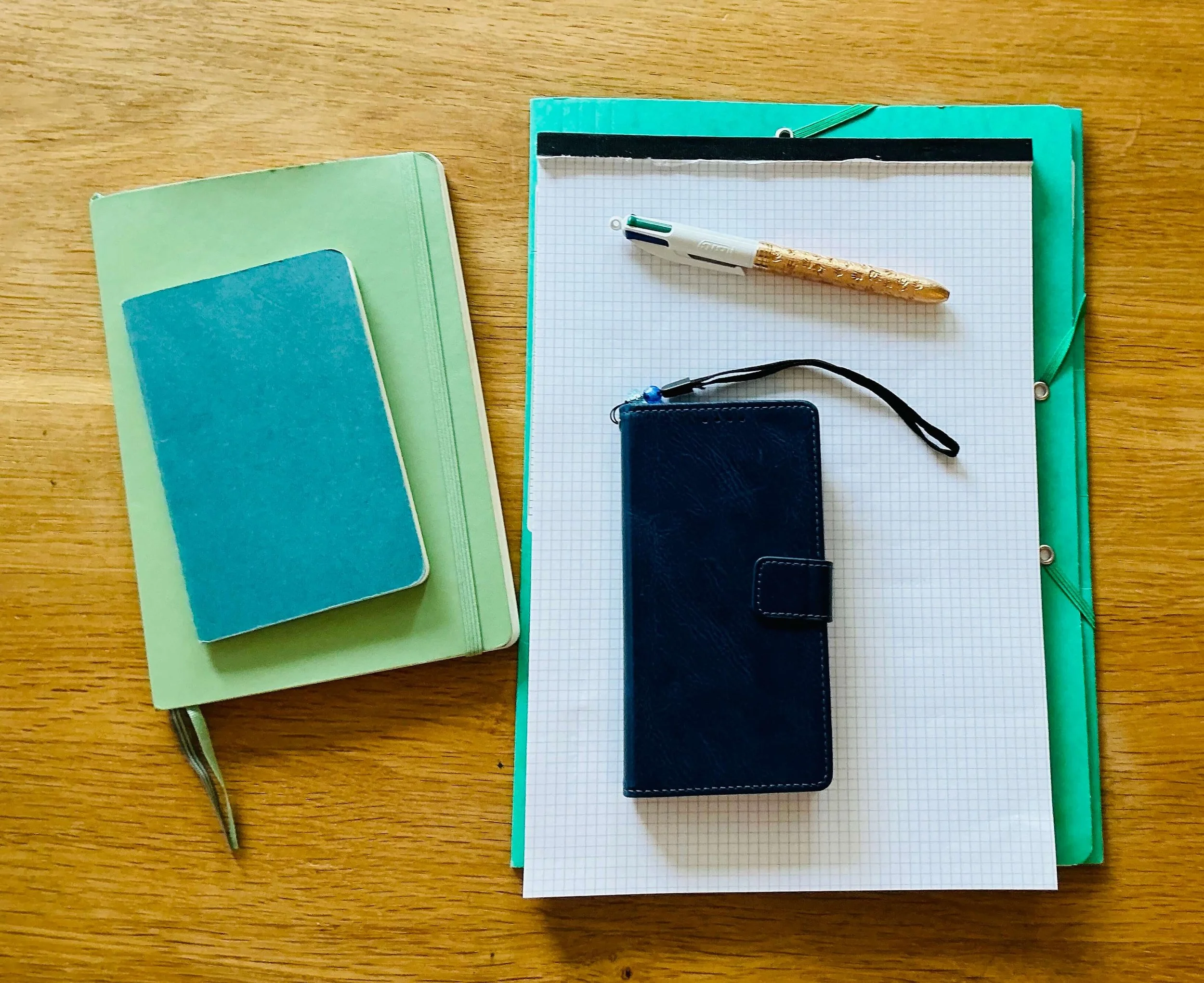 Une table en bois avec plusieurs carnets de notes de Emilie Stein, psychologue FSP formée aux TCC, un stylo, une petite pochette et une feuille quadrillée.