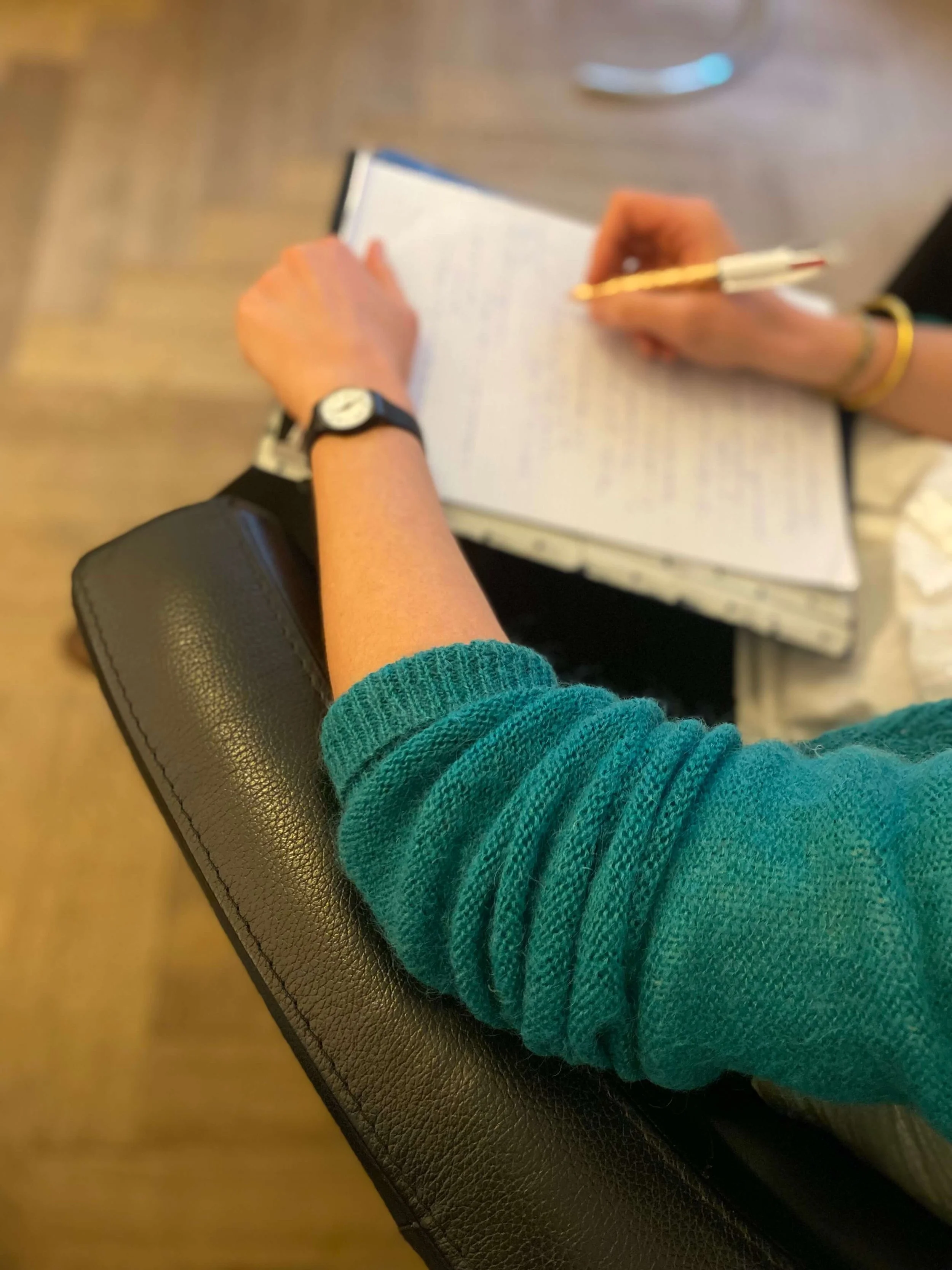 Emilie Stein, psychologue FSP, dans son cabinet à l'avenue de la gare à Lausanne, assise, portant un pull vert et un montre noire, en train de prendre des notes ou écrire dans un carnet blanc.