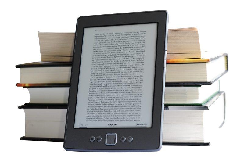 An image of an ebook reader in front of a stack of paper books