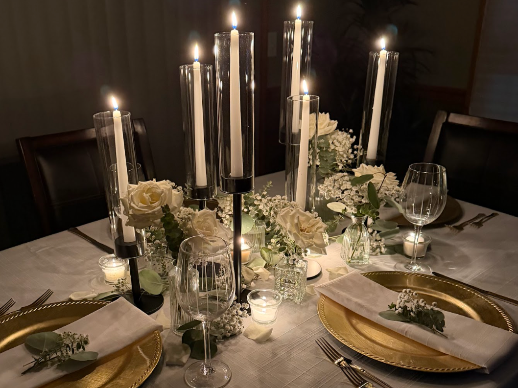 Elegant dining table decorated with white roses, baby's breath, and candles in glass holders, set for a formal dinner.