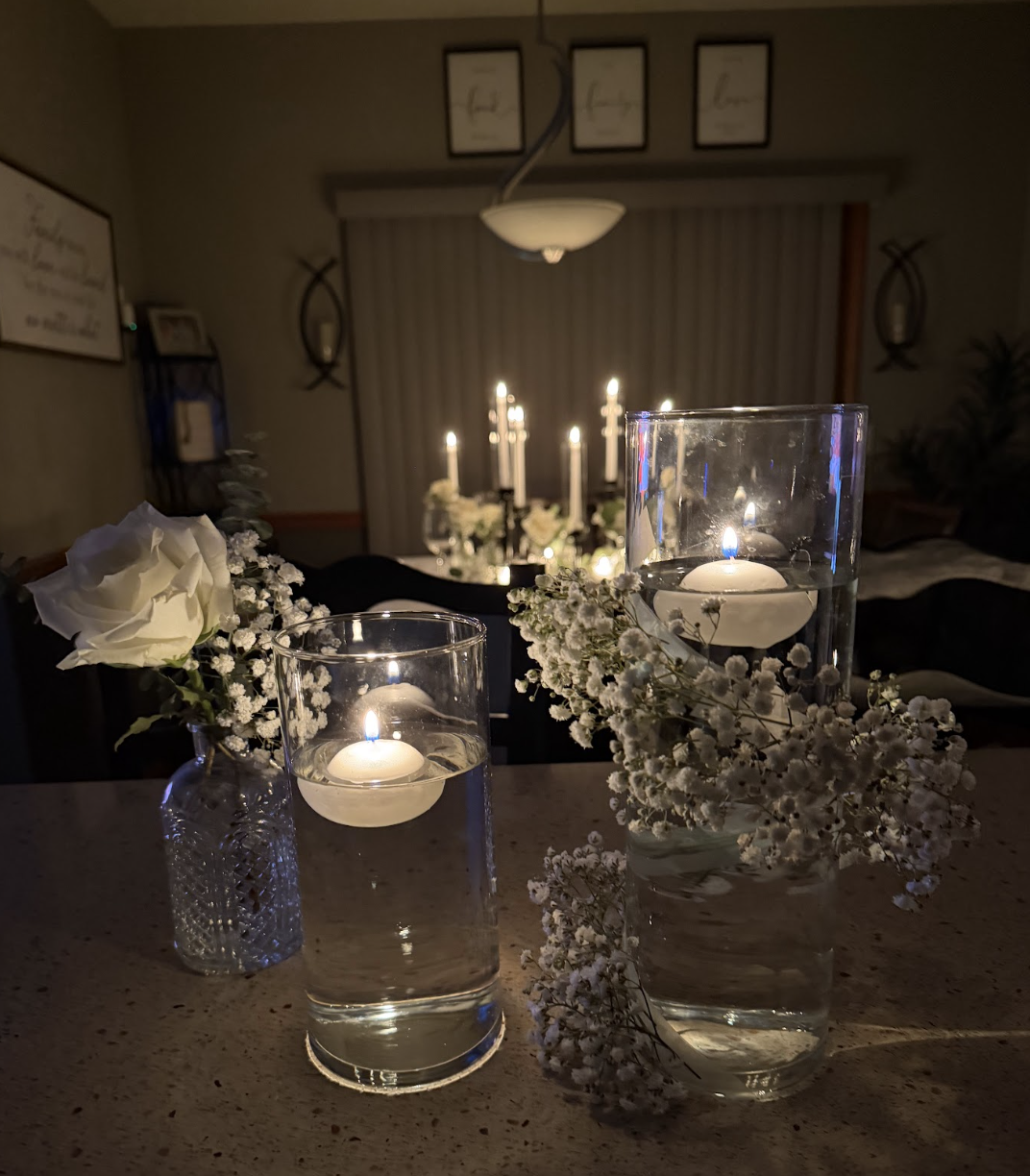 Several glass containers with floating candles and flowers on a table at night