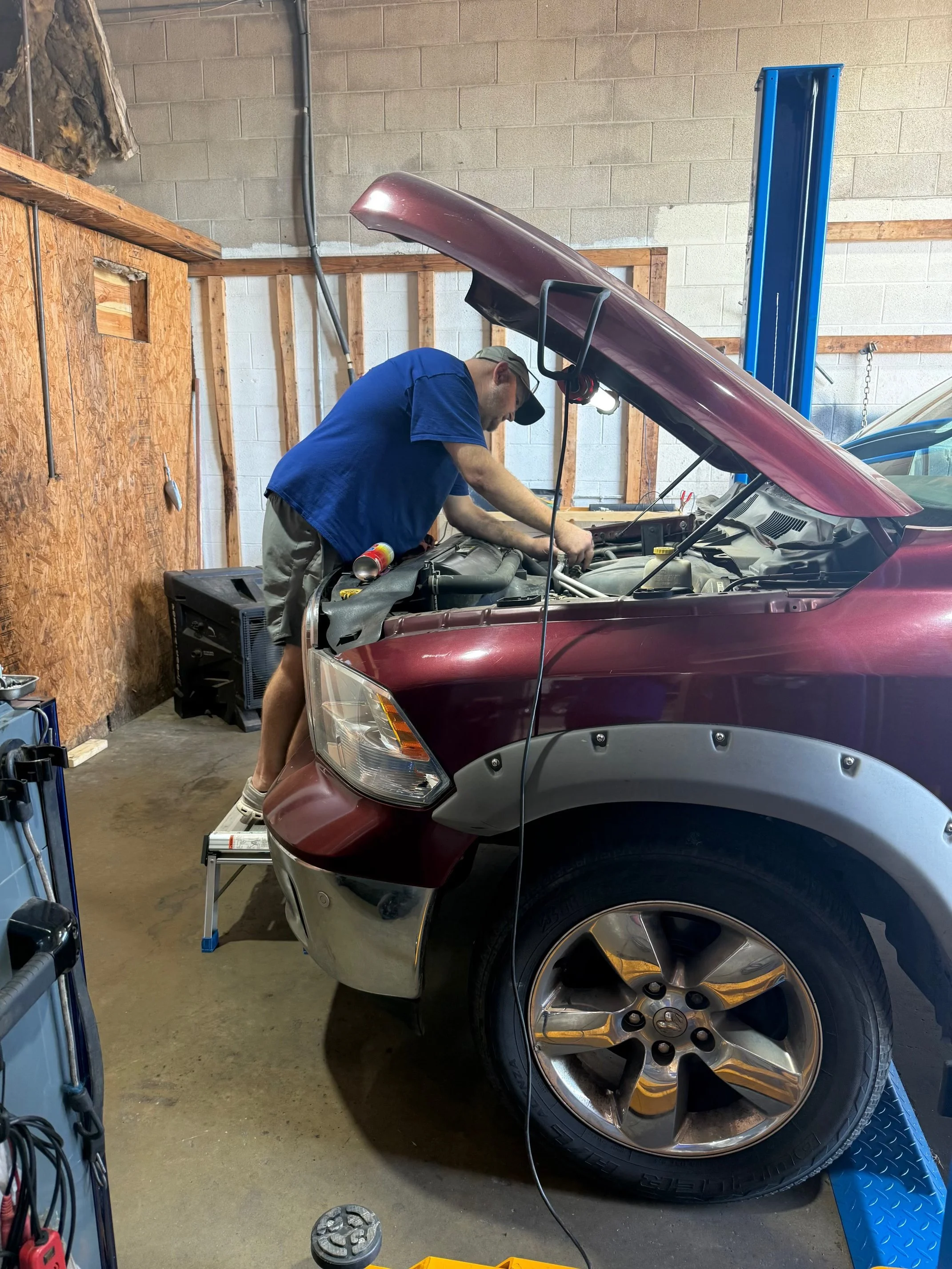 A man working on a red car with the hood open inside a garage.