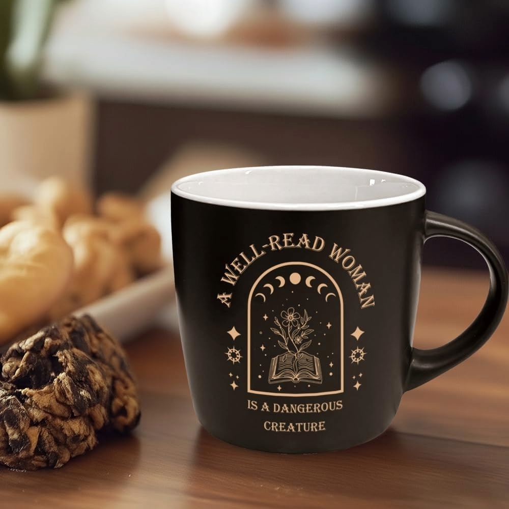 Black bookish mug reading “Well-read women are dangerous” sits on a wooden table beside pastries, creating a cozy, literary atmosphere.
