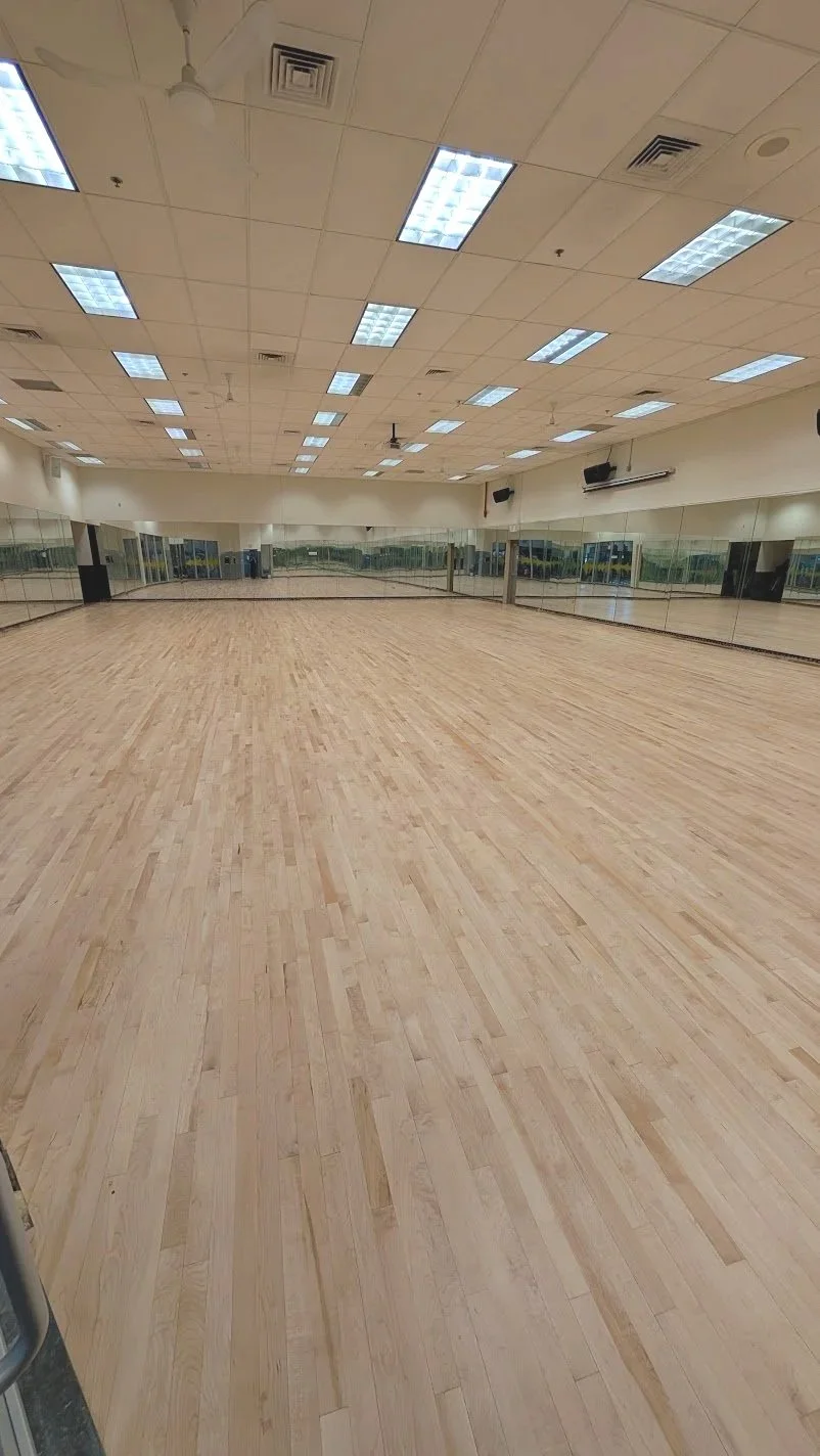Empty dance studio with hardwood floors, large mirrors on the walls, and ceiling lights. In Denver Cherry Creek Wash Park.