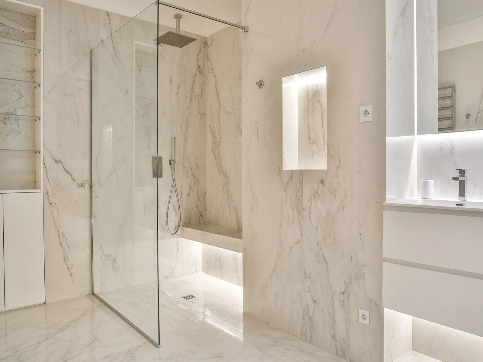 Modern bathroom with marble walls, shower area with glass partition, wall-mounted sink, and minimalistic decor.