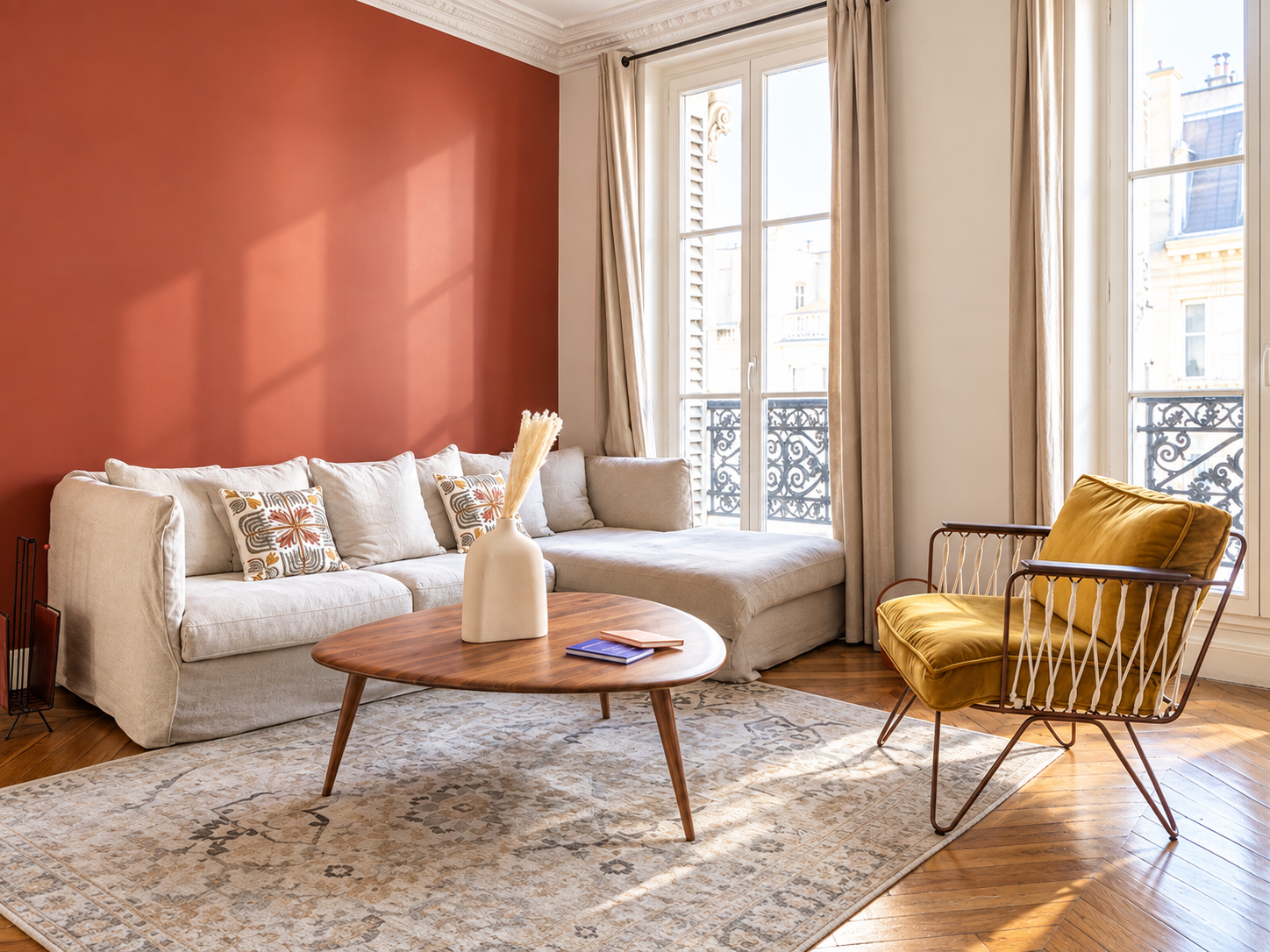 Living room with white sectional sofa, patterned pillows, wooden coffee table with a white vase and books, yellow armchair, large windows with curtains, hardwood floors, and a beige rug.