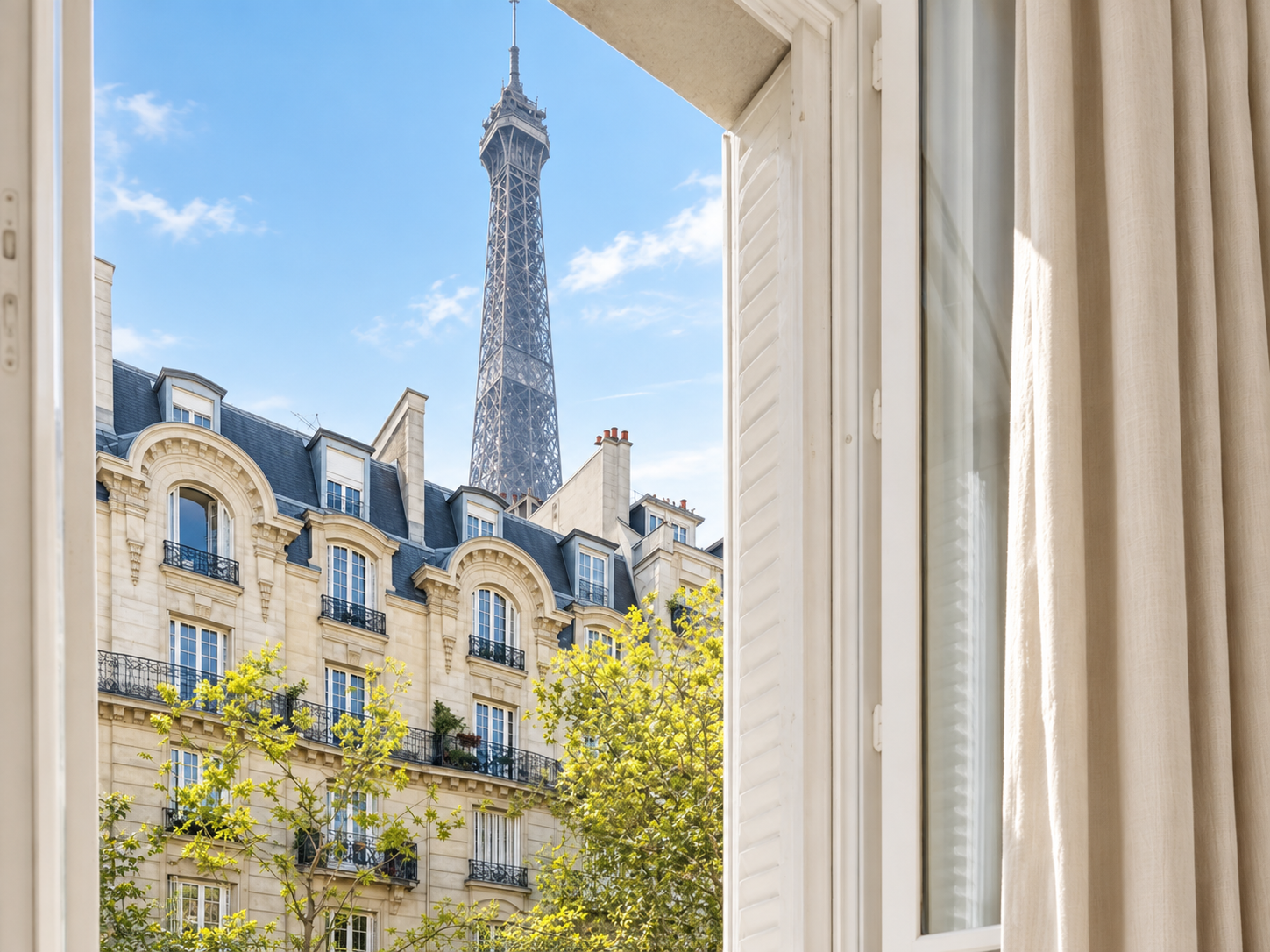 View of Parisian-style building with trees, and Eiffel Tower in the background seen through an open window with beige curtains.