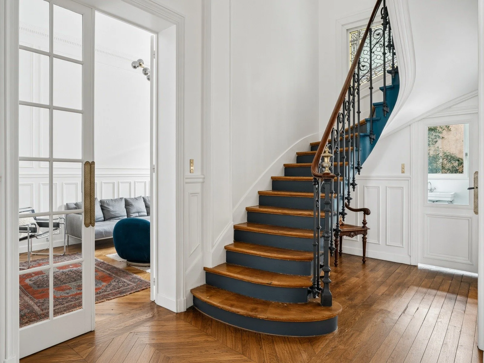 Interior view of a home with a curved staircase, white walls, hardwood floors, and adjoining rooms visible through doorways and windows.