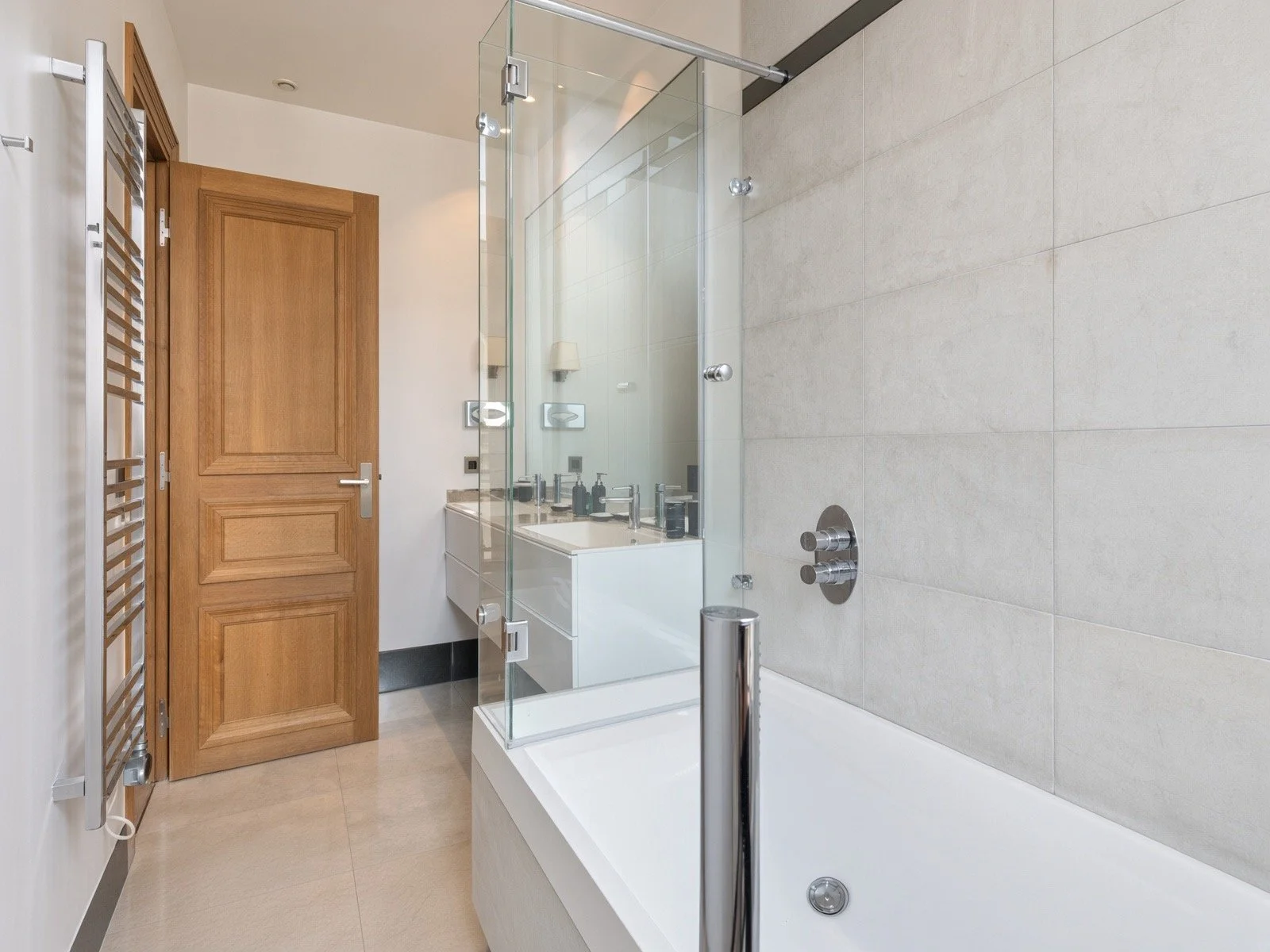 Modern bathroom with a bathtub, glass shower enclosure, wooden door, white vanity with a mirror, and a wall-mounted towel rack.