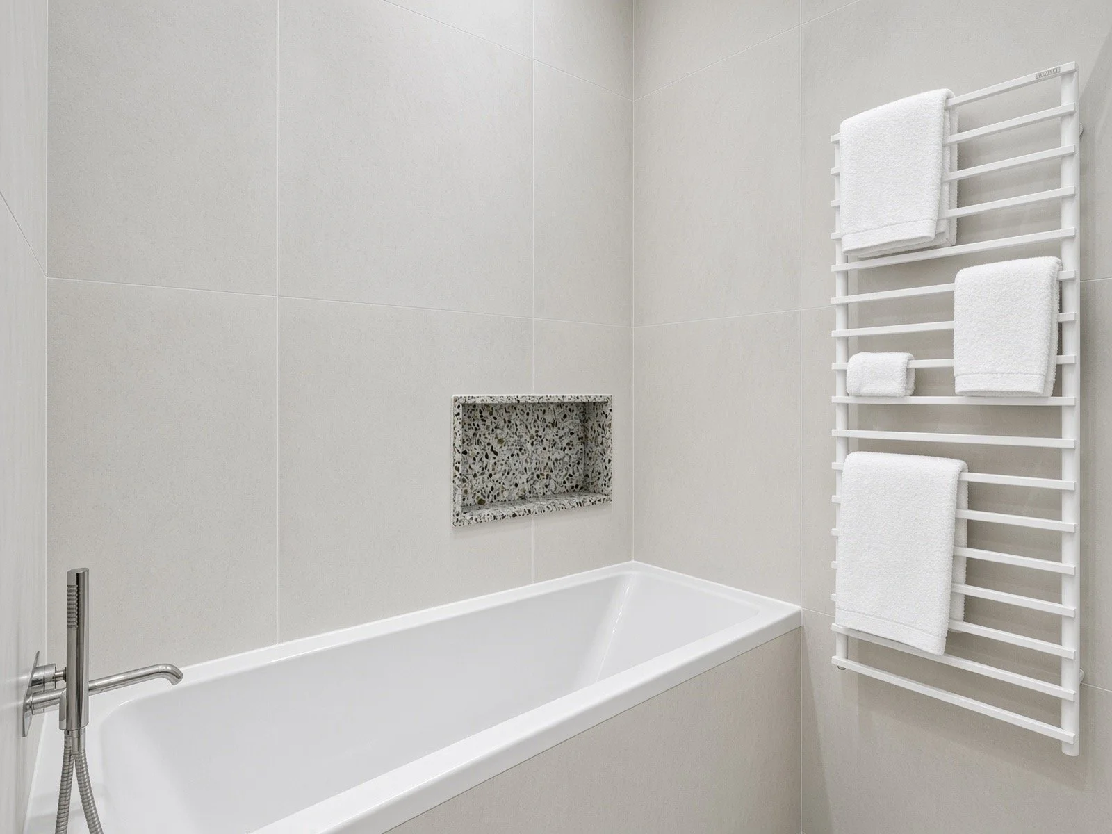 A modern bathroom with a white bathtub, a built-in pebble stone shelf in the wall, and a white towel rack with towels on it.