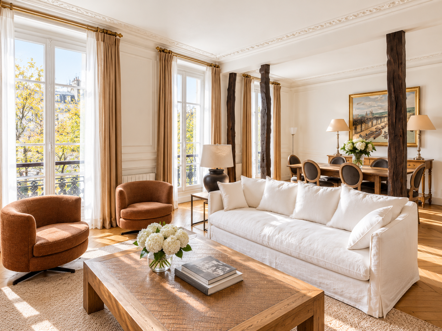 Living room with large windows, beige curtains, white walls, wooden flooring, and minimalistic furniture. Features a white sofa, two orange armchairs, a wooden coffee table with a flower vase, a wooden dining table with six chairs, and various lamps. Artwork hangs on the wall.