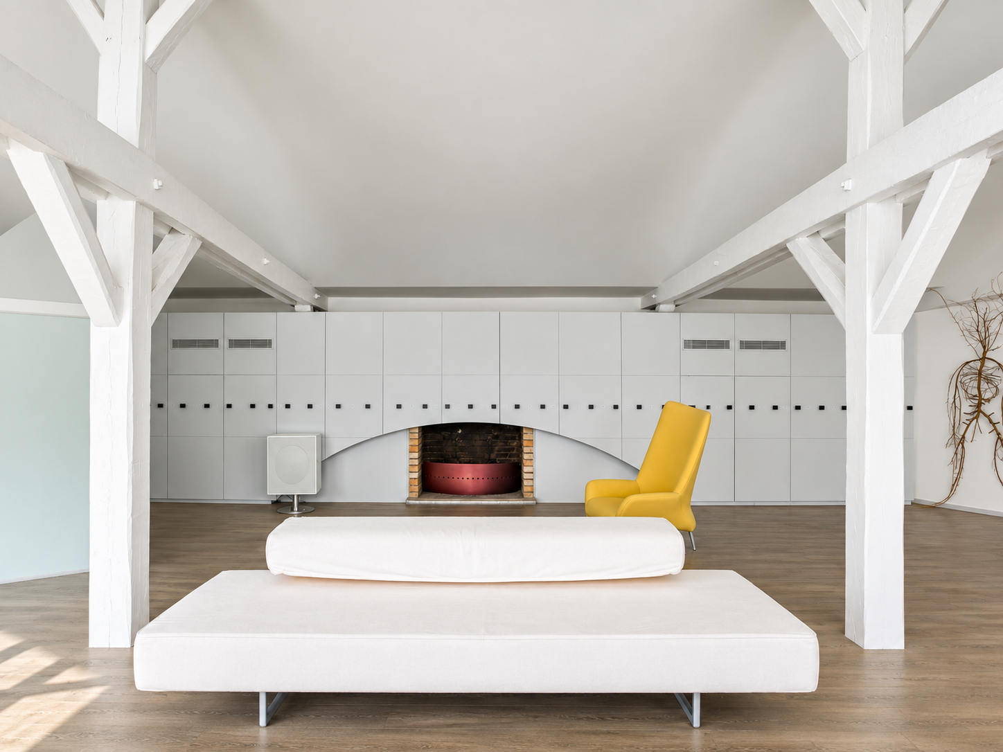 Modern living room with white walls, a white couch in the foreground, a yellow armchair, and a fireplace with dark bricks surrounded by white cabinetry.