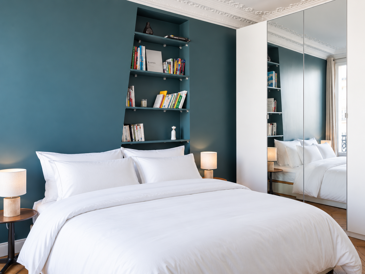 A modern bedroom with a white bed, teal accent wall, built-in bookshelf, mirrored closet, and a window with curtains.