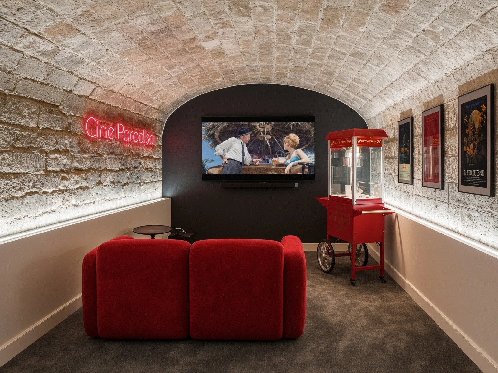 A cozy, dimly lit movie viewing room with a red couch, a small side table, a popcorn cart, and framed posters on the wall. A neon sign reads 'Ciné Paradiso' and a large screen displays a scene from a black-and-white film.