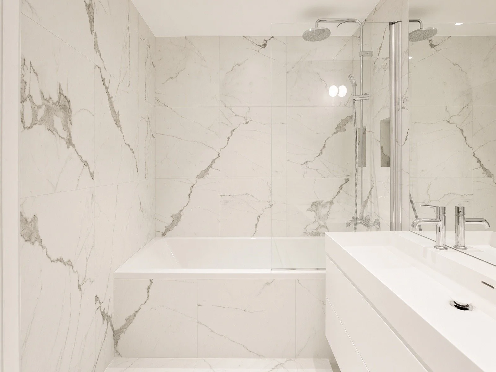 Modern bathroom with marble walls, a built-in bathtub, a glass shower enclosure, a sink with a chrome faucet, and minimalistic fixtures.