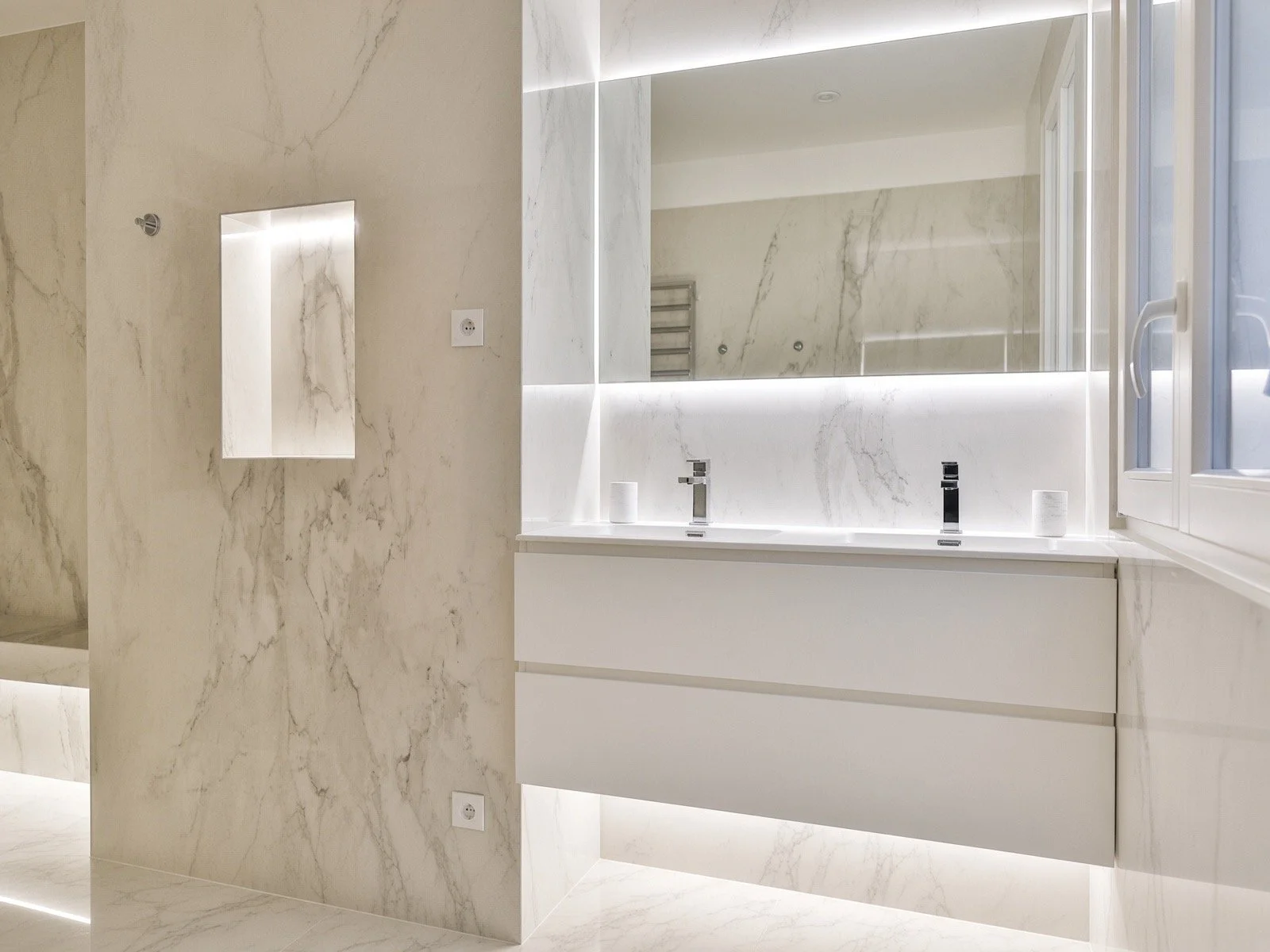 Modern bathroom with marble walls, a double sink vanity, and a large mirror with integrated lighting.