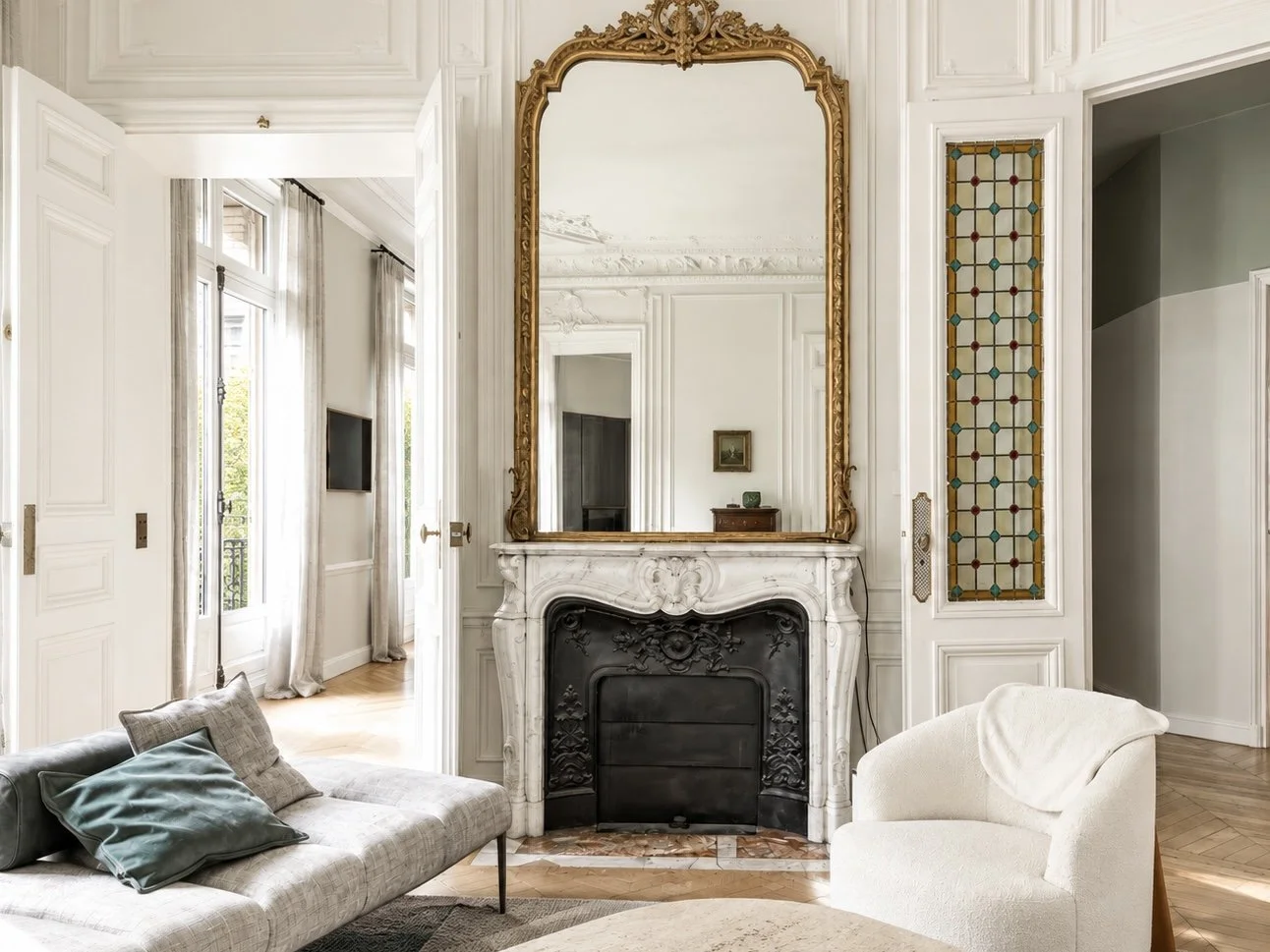 Elegant living room with ornate white fireplace, gold-framed mirror, and beige seating.