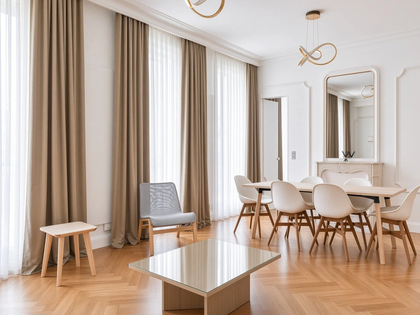 Modern dining room with beige curtains, a wooden table with white chairs, a gray armchair, and a large mirror on white walls, natural light coming through sheer curtains.