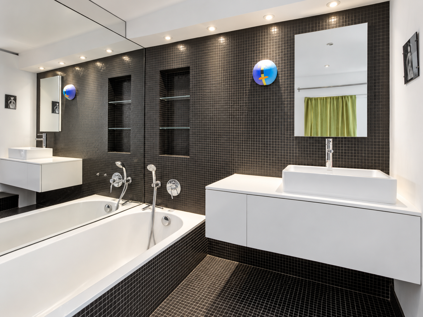 Modern bathroom with black tiled walls and floor, a white bathtub, two white sinks with mirrors, built-in shelves, and green curtains.