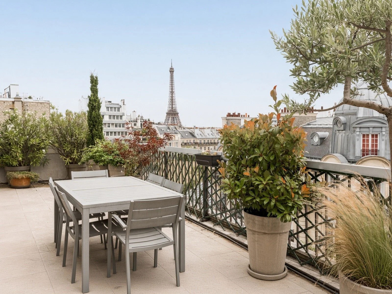 Paris cityscape view from a rooftop terrace with outdoor furniture and potted plants, including the Eiffel Tower in the background.