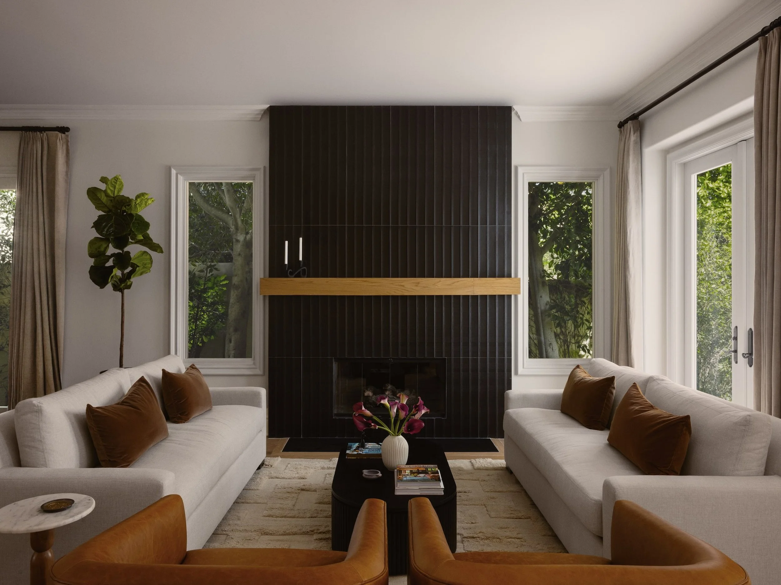 Living room with white sofas, orange pillows, black coffee table with magazines, potted plant, and large windows with curtains showing greenery outside.
