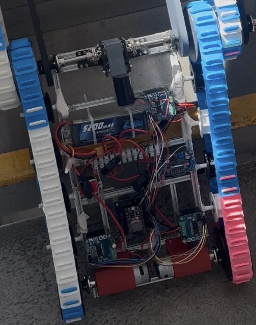 Robot with blue and pink treads, encased in an open metal framework, featuring wires, circuit boards, and motors.