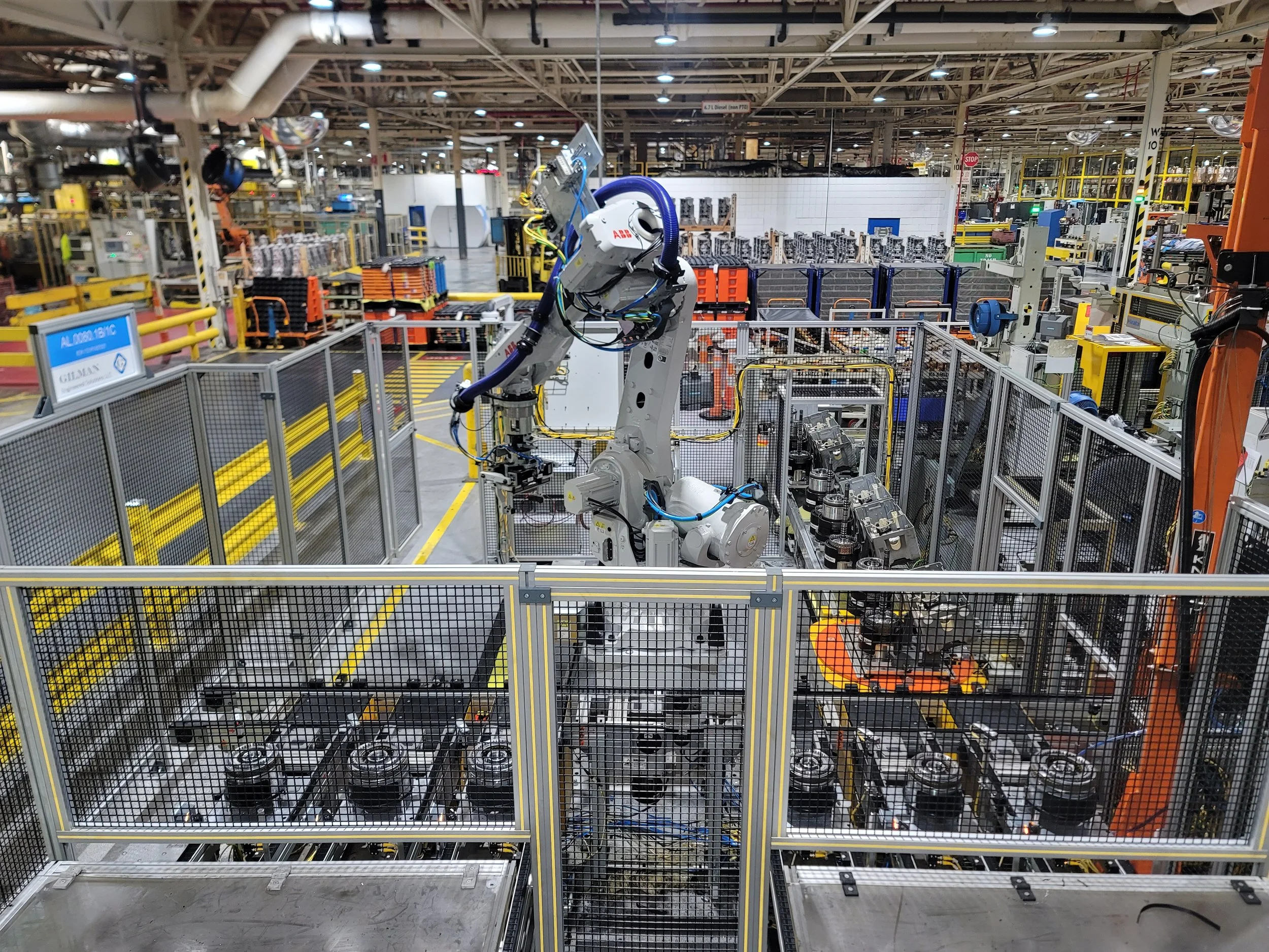 A robotic arm working inside an industrial manufacturing facility, surrounded by safety barriers and various machinery and equipment.