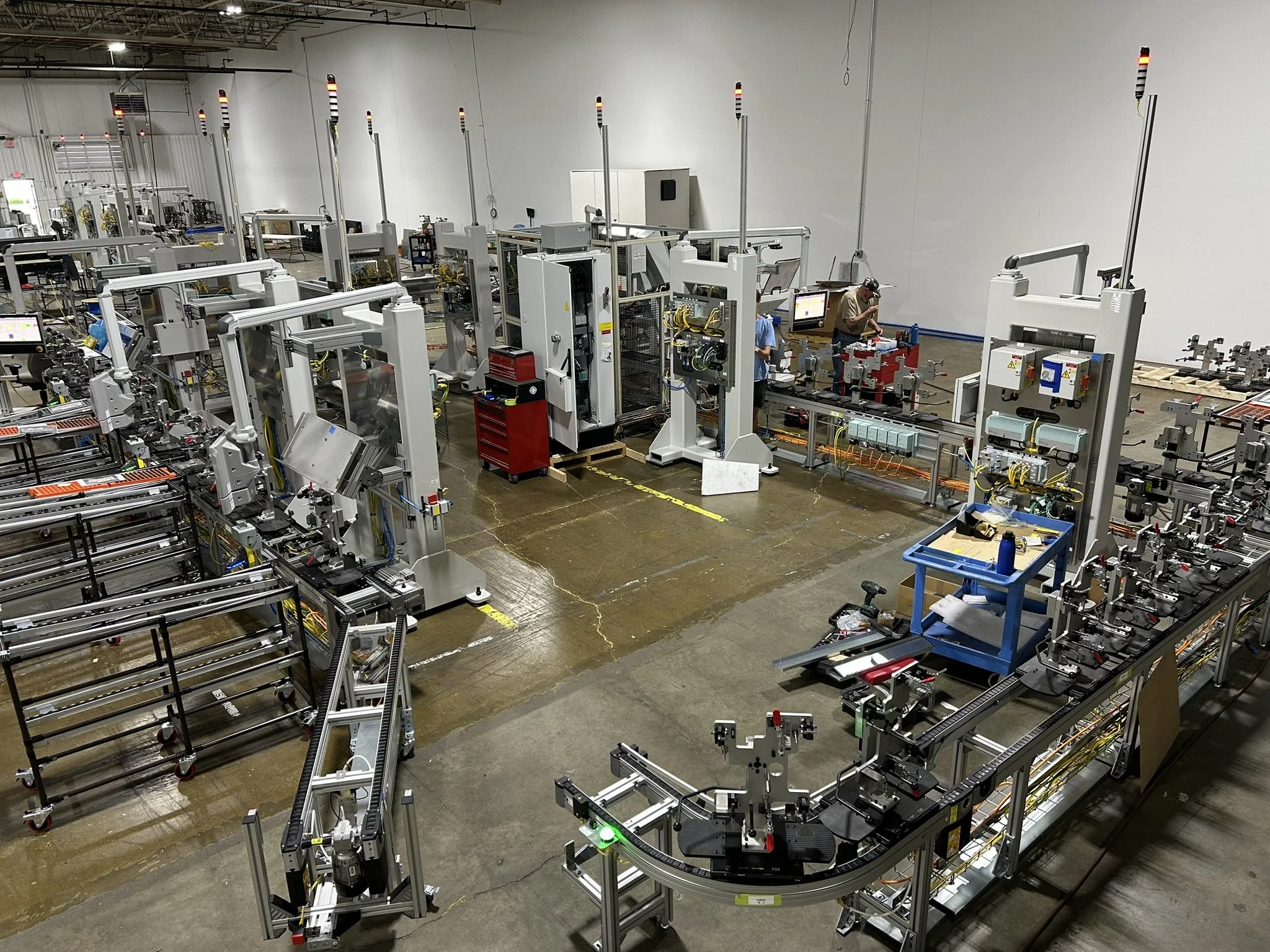 Inside a manufacturing facility with multiple robotic automation machines and conveyor belts, with workers operating or checking the equipment.