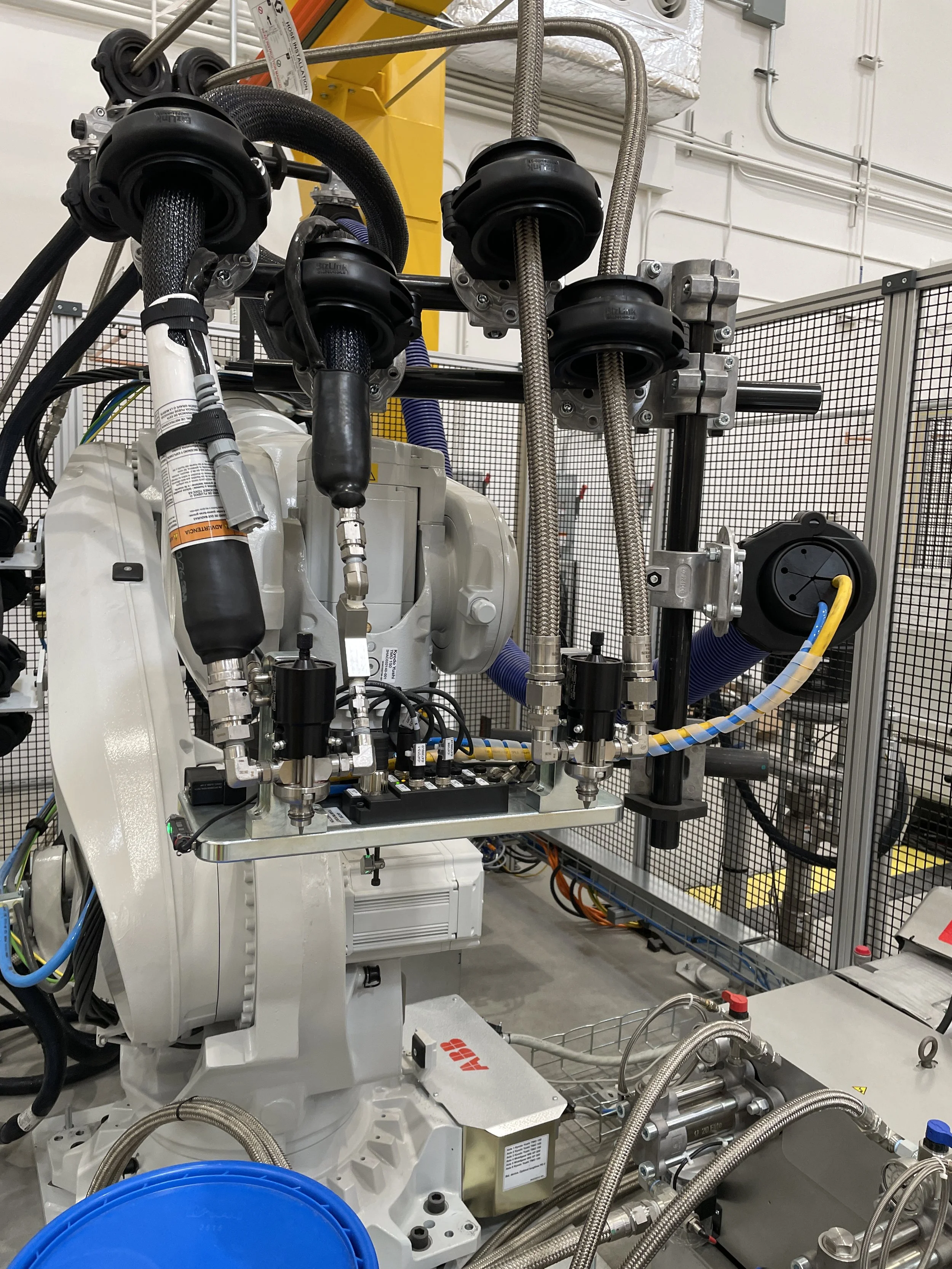 Industrial machinery with black flexible pipes, metal rods, and various control knobs, situated in a laboratory or manufacturing setting.
