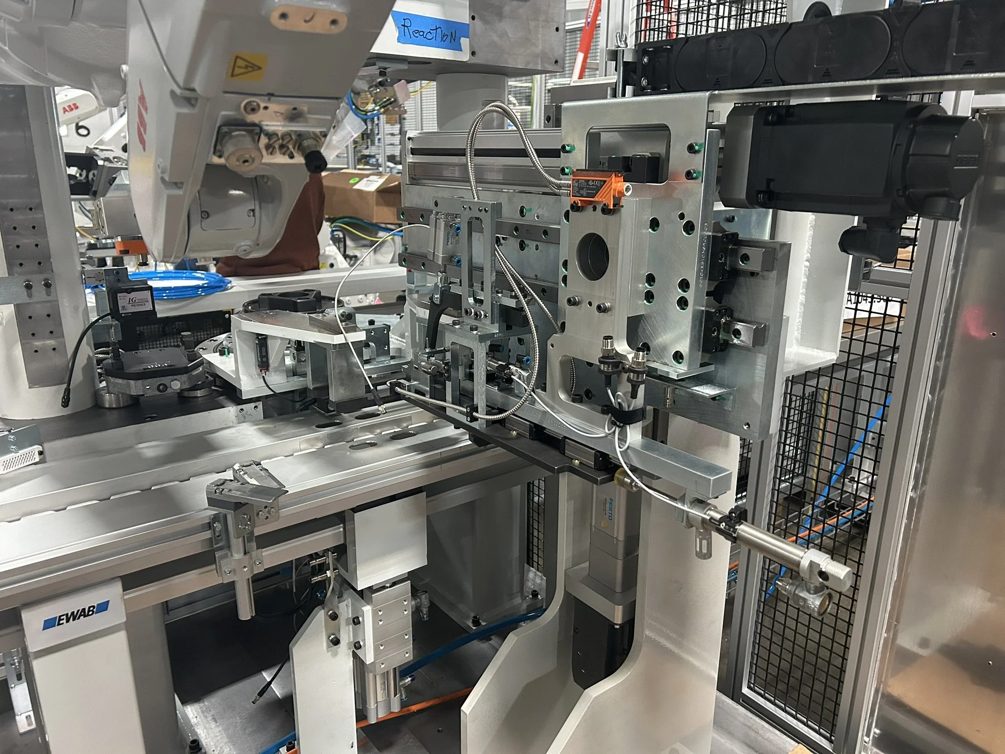 Inside a laboratory or manufacturing setting with machinery and equipment, including a labeled reaction component, metallic framework, wires, and control modules.