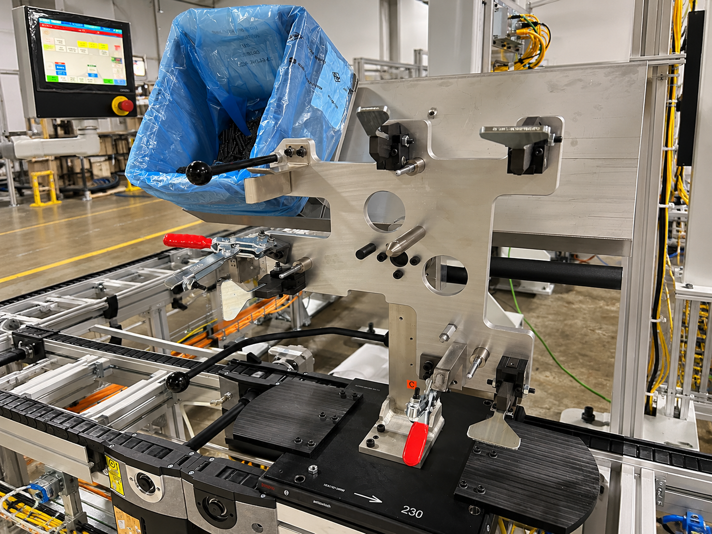 Industrial machinery in a manufacturing setting with conveyor belts, metal components, and a computer screen displaying a control interface.