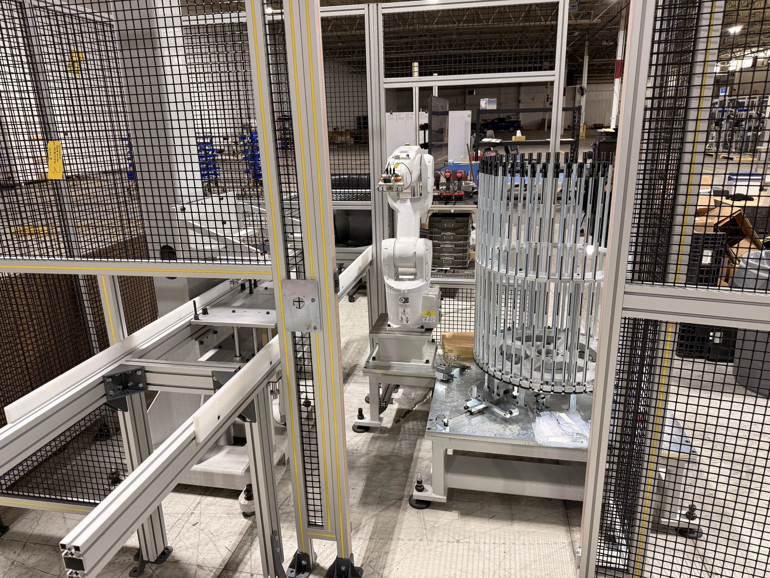 Robotic arm inside a manufacturing enclosure with metal frames and safety nets in a warehouse or factory.