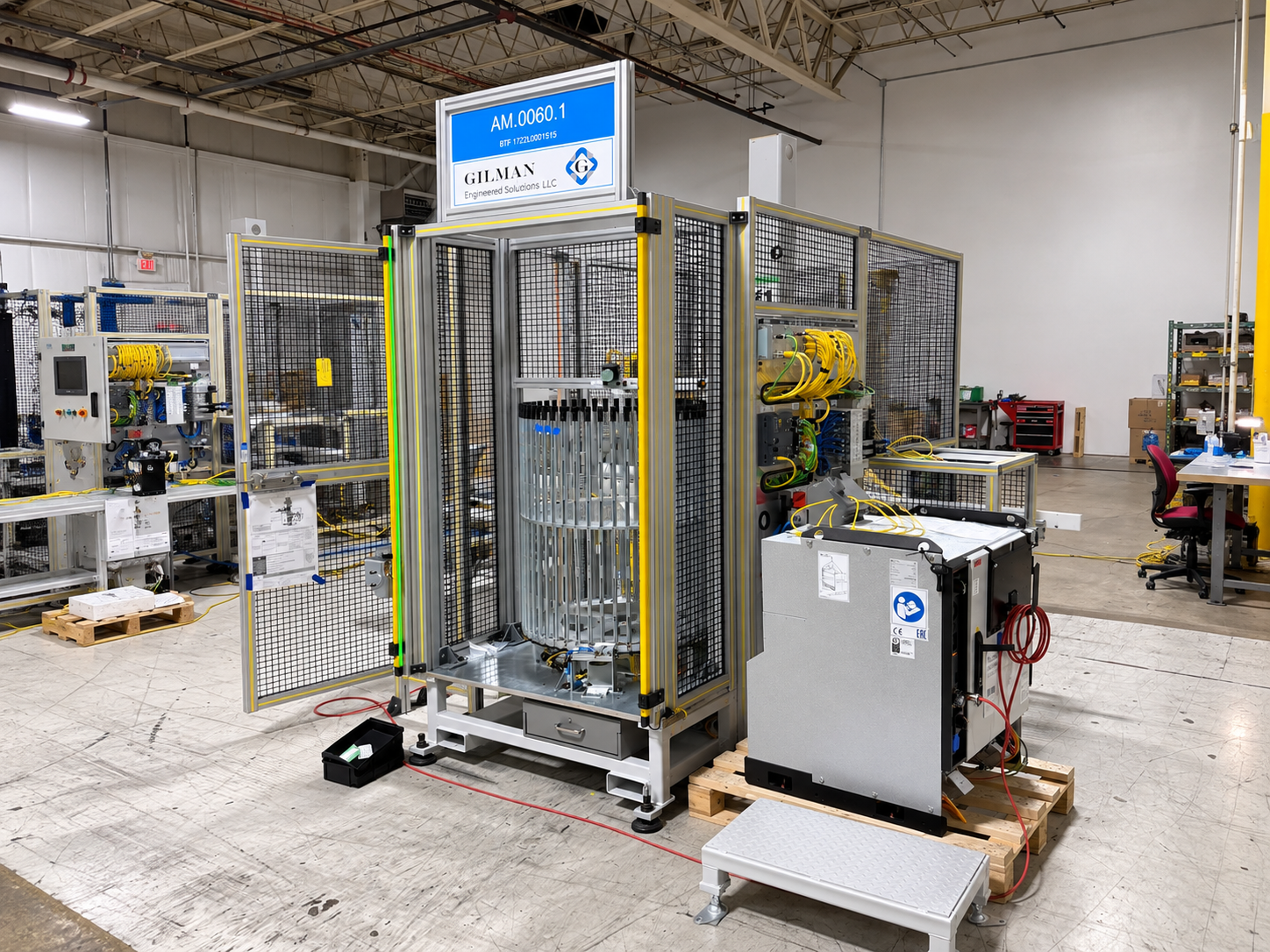 Industrial testing machine enclosed in a metal safety cage in a factory setting with various tools and equipment nearby.