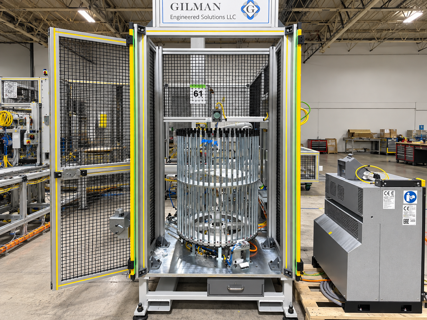 Industrial machinery in a factory with a metal cage structure, cables, and control units, in a spacious workspace with workbenches and equipment in the background.