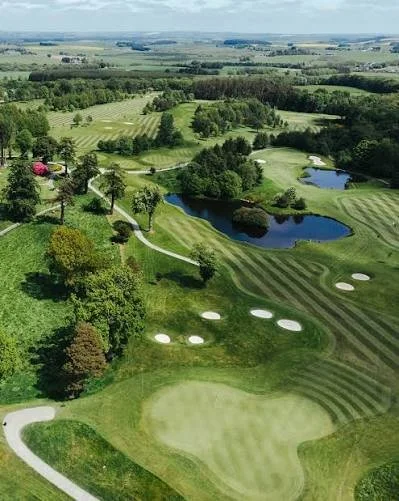 Aerial view of a golf course with fairways, greens, sand traps, water hazards, and surrounding trees.