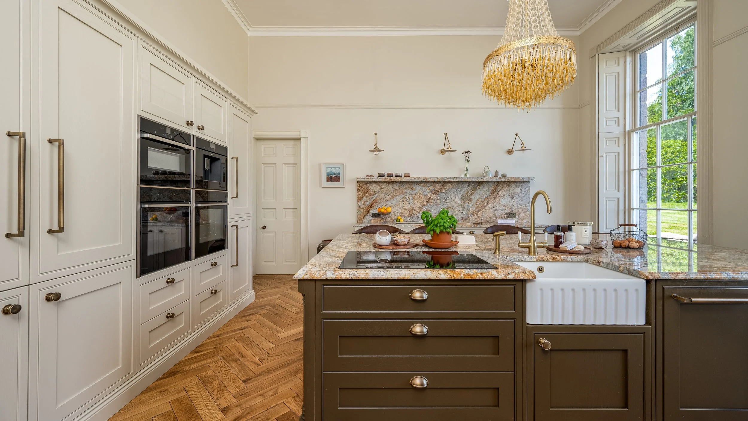 A kitchen with white cabinetry, a granite island, a granite wall, a large window, and a chandelier.