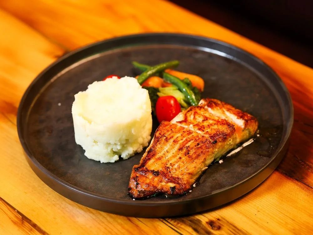 Grilled salmon fillet with mashed potatoes and mixed vegetables on a black plate.