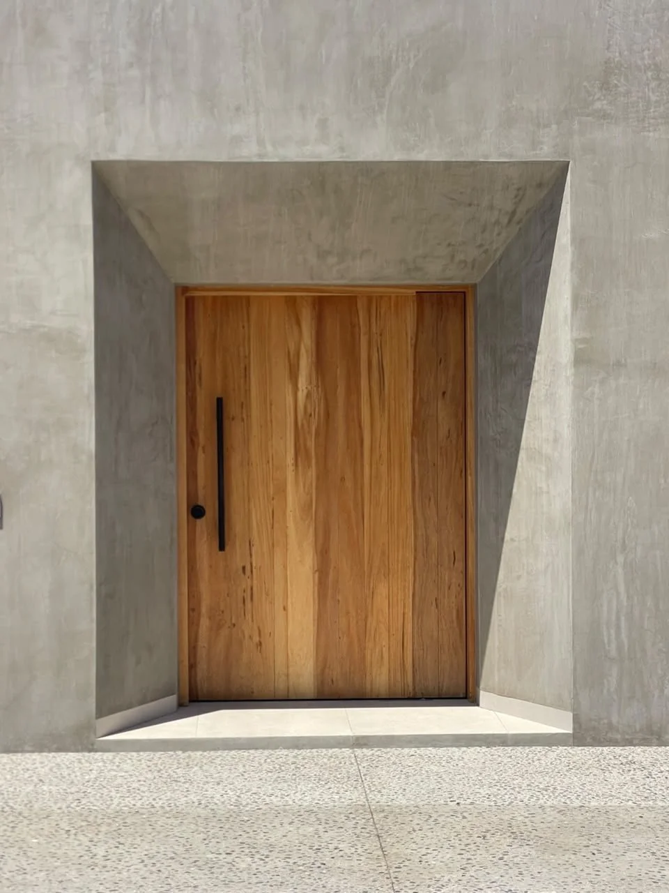 A wooden door set into a concrete wall with a geometric, sunken frame around it.