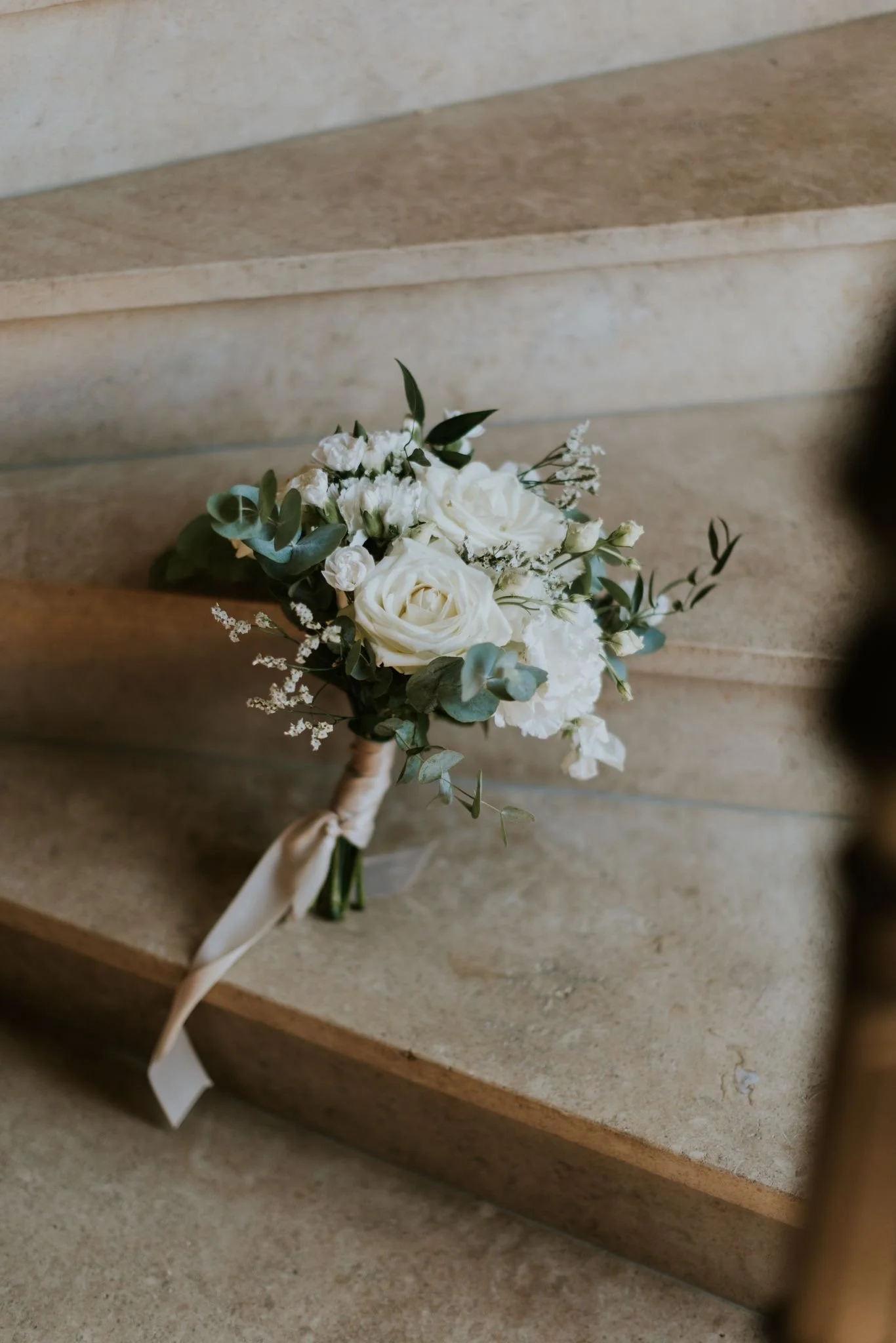 Un bouquet de fleurs blanches avec des feuilles vertes, posé sur des marches en pierre.