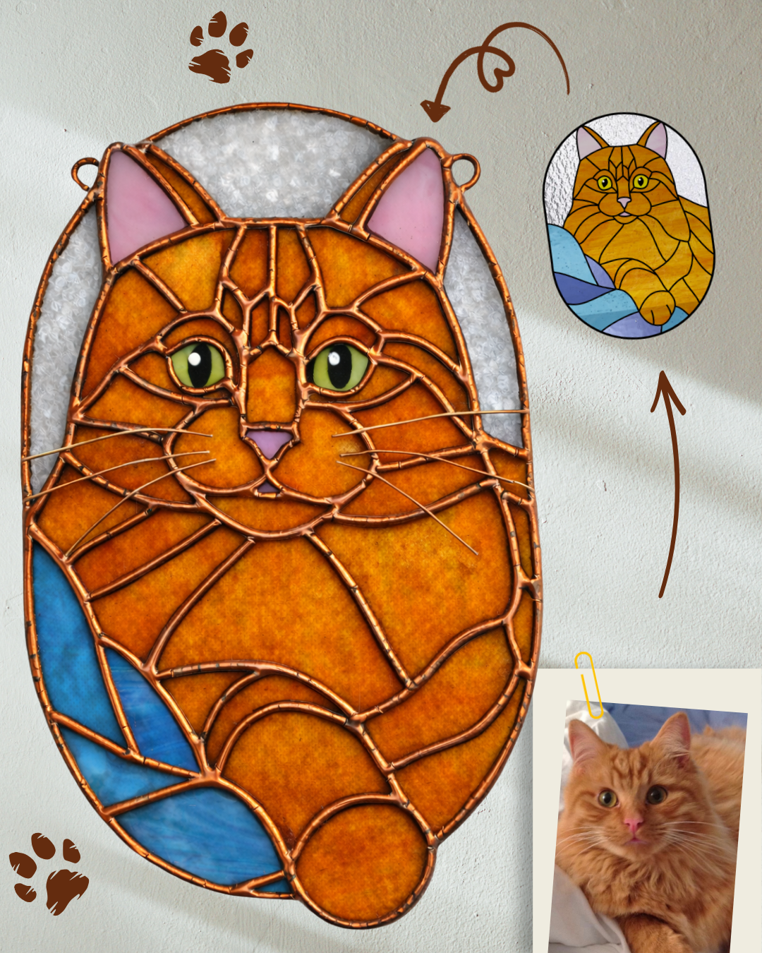 A stained glass art piece of a cartoon orange cat with green eyes, pink nose, and a fish tail, hung on a wall. There is a small photo of a real orange cat taped below with a gold paper clip. The wall has paw print decorations and a drawing of a cat.