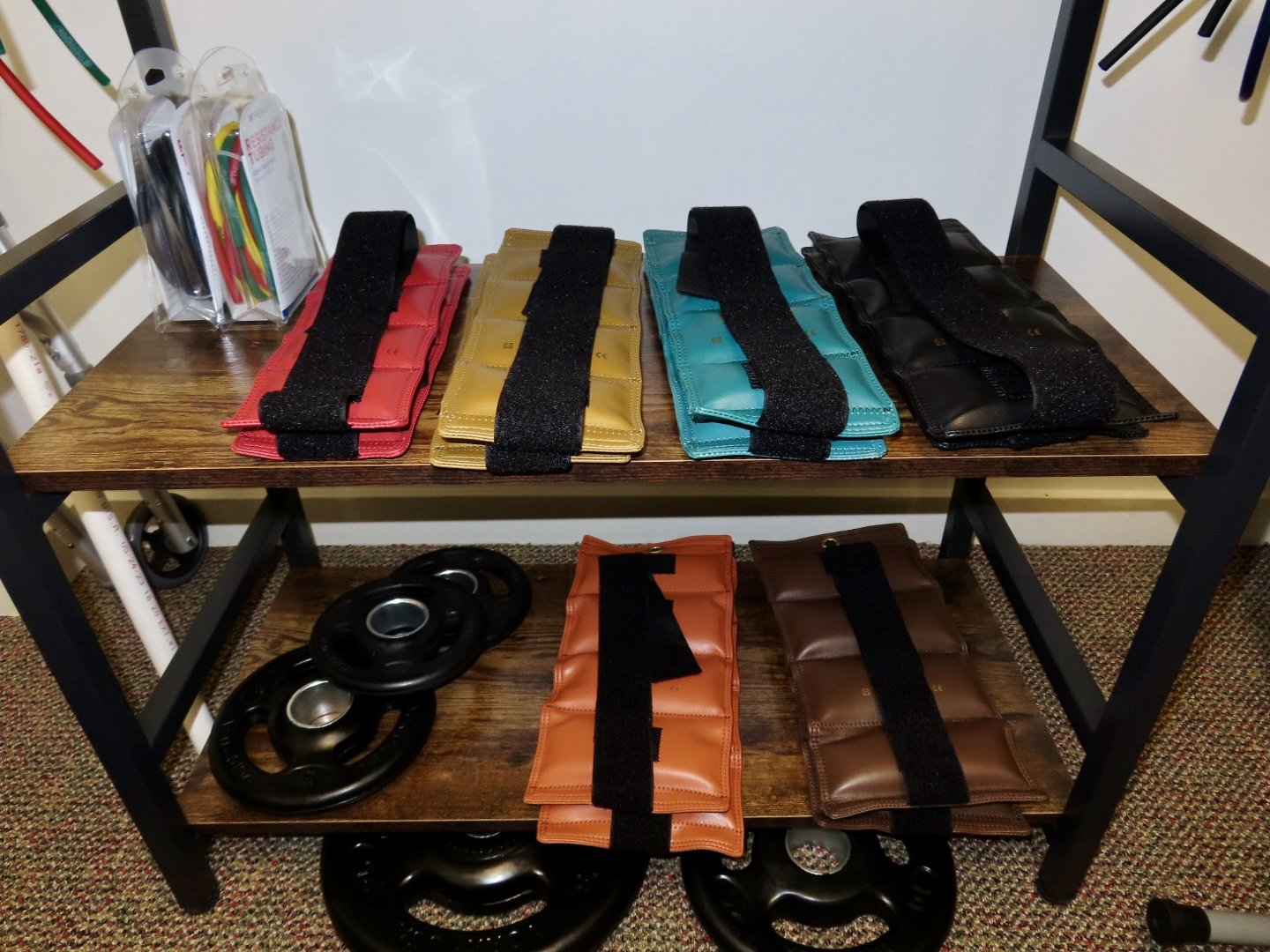 Colorful resistance band handles and weights on a wooden gym rack.