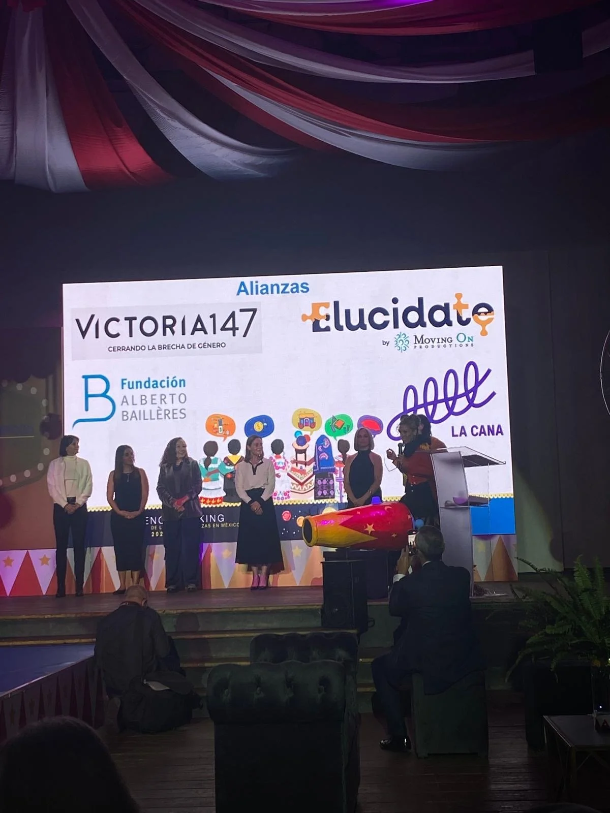 Women standing onstage at an awards event beneath a screen displaying alliance logos, including Victoria147, Lucidate, Fundación Alberto Baillères, and La Cana.
