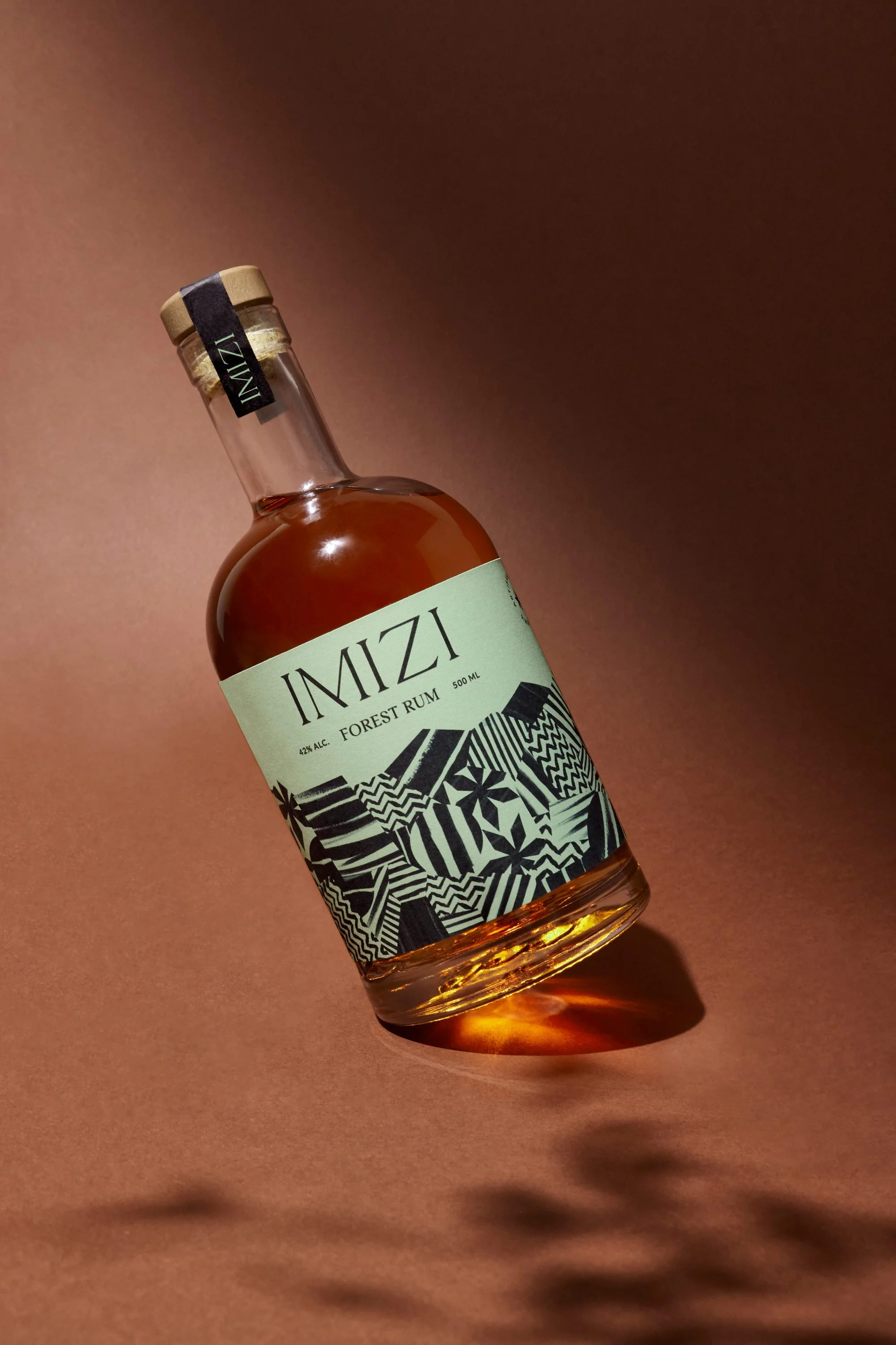 A bottle of IMIZI Forest Rum with a black and white abstract patterned label, set against a pinkish background.