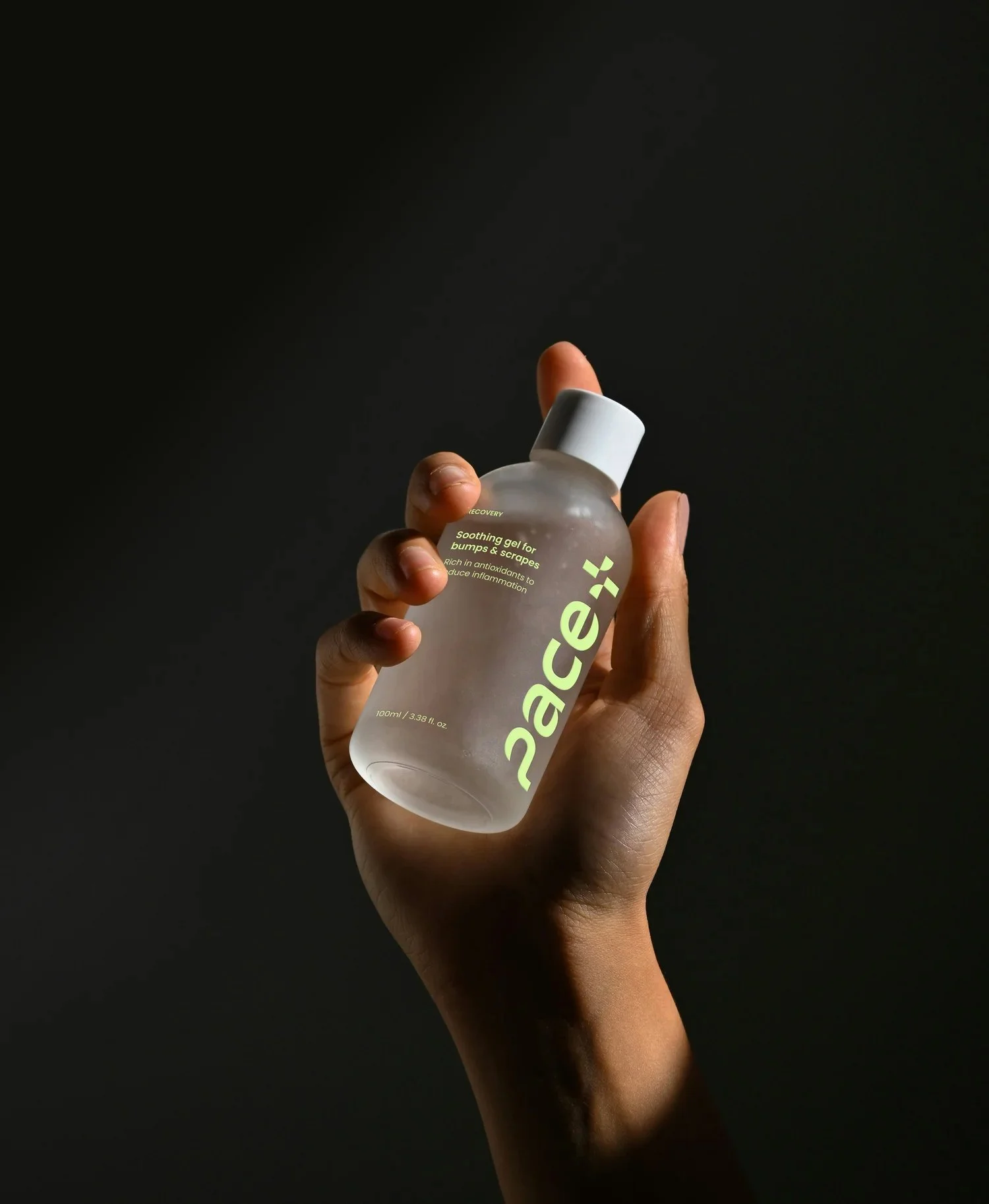 Hand holding a translucent bottle of face gel against a black background.