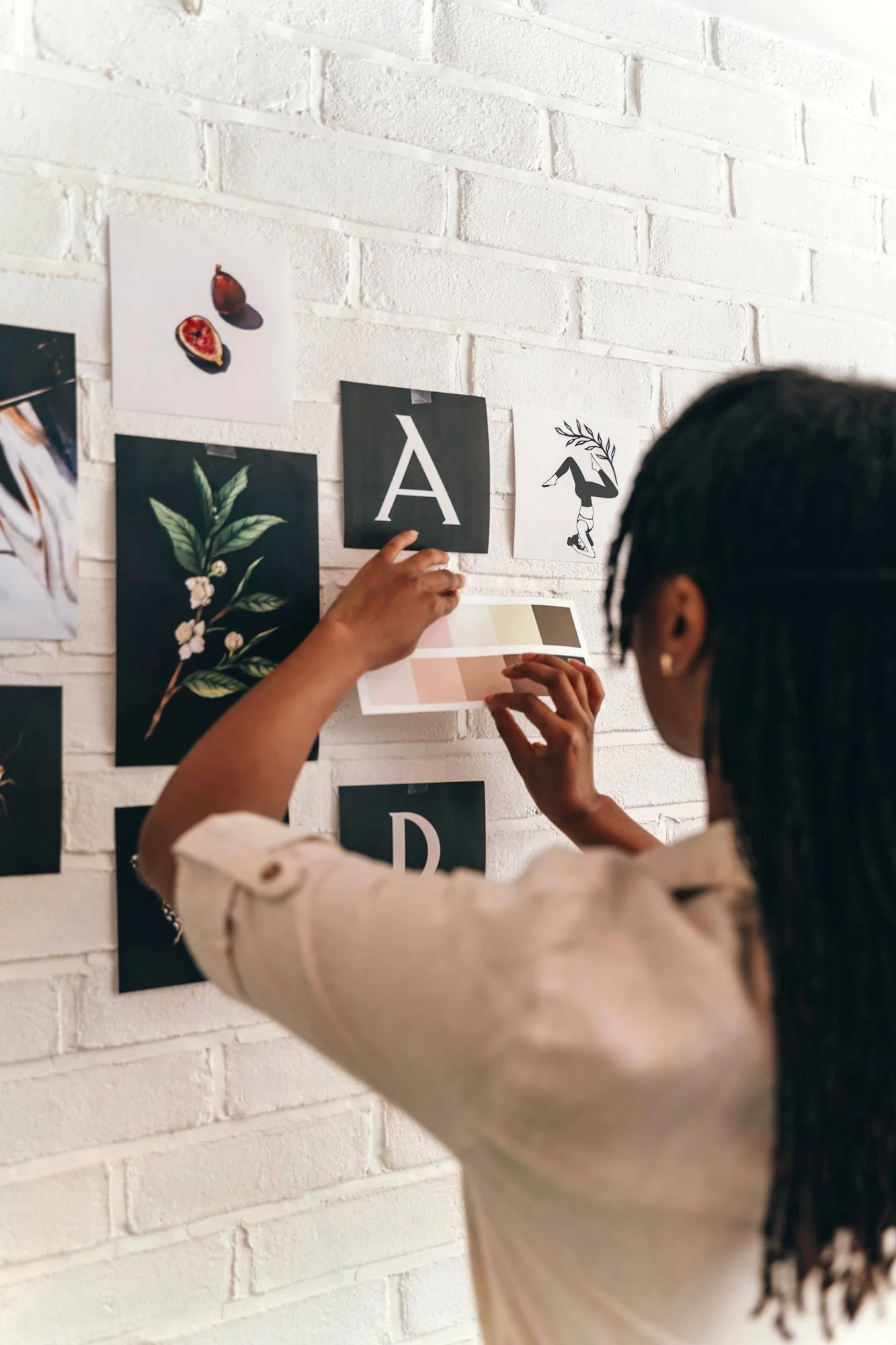 A woman arranging printed brand design elements on a white brick wall.