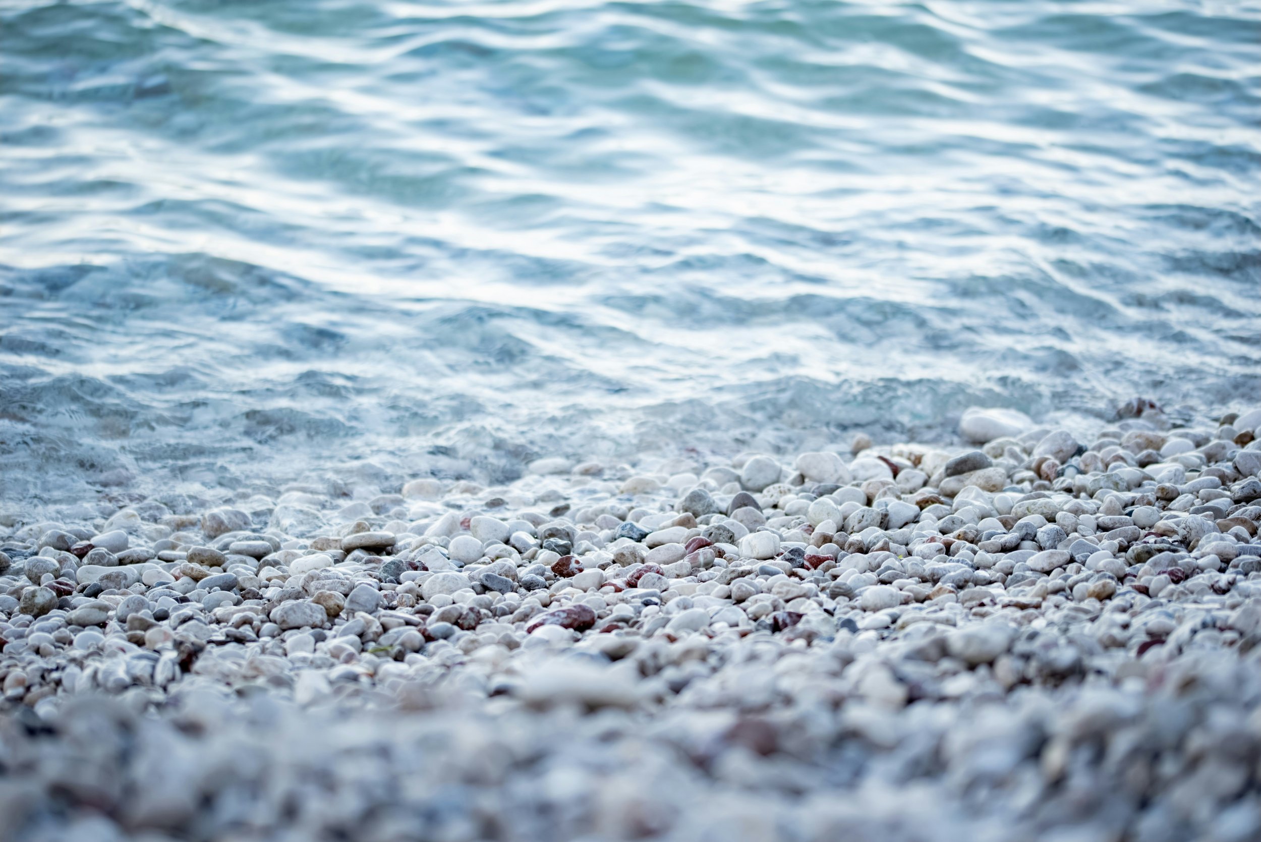 Close-up view of a pebbled beach with small white and colored stones, and gentle waves lapping at the shoreline.