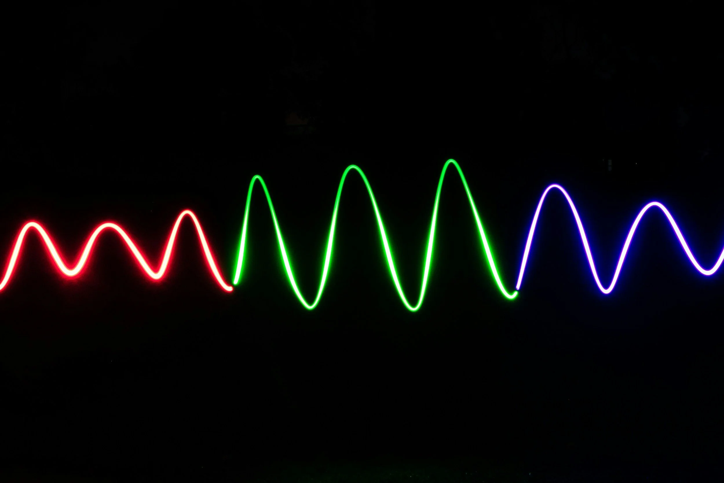 Colorful neon light waviness pattern on a dark background with red, green, and blue lines.