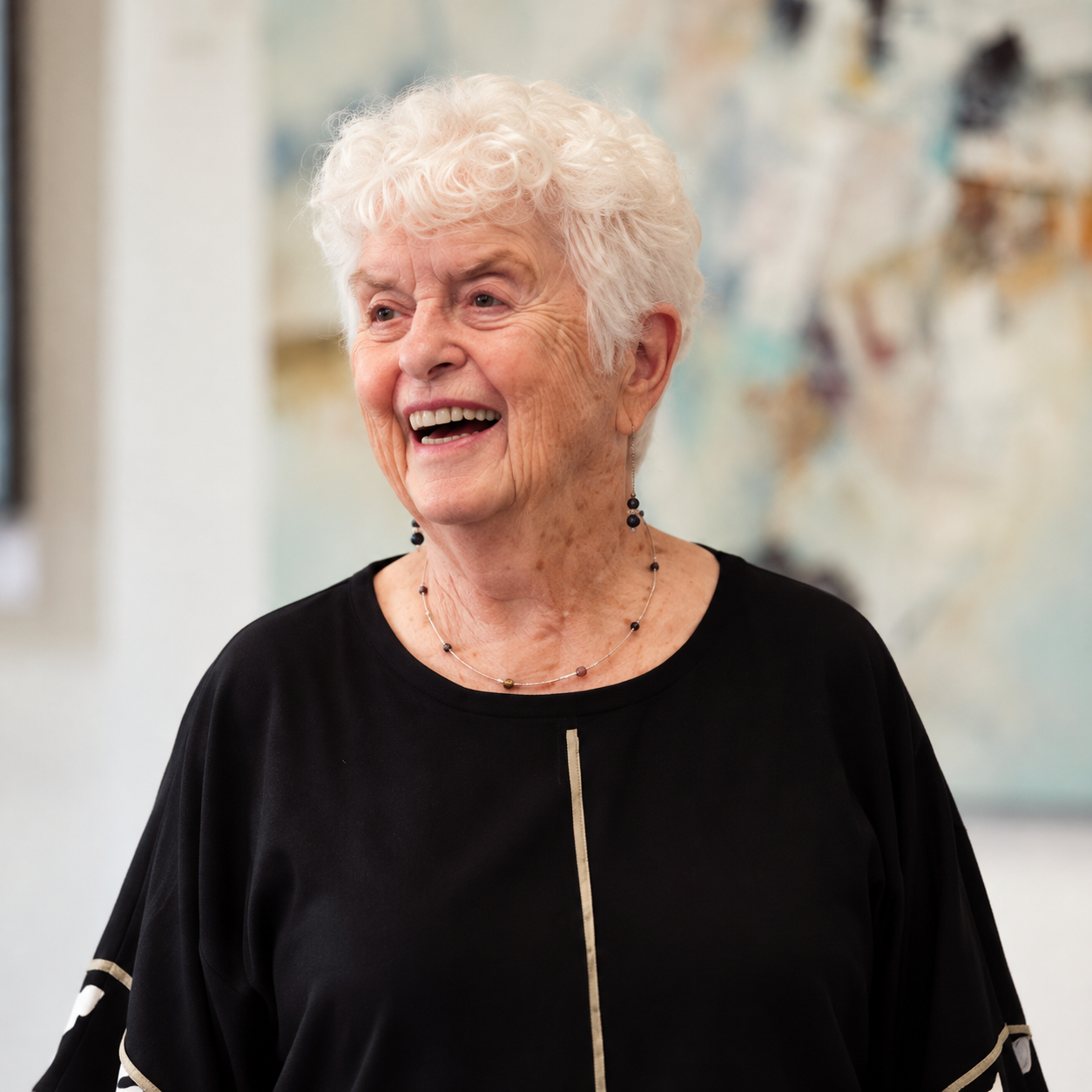 Smiling Mary Alice Braukman with curly white hair wearing a black blouse and beaded necklace